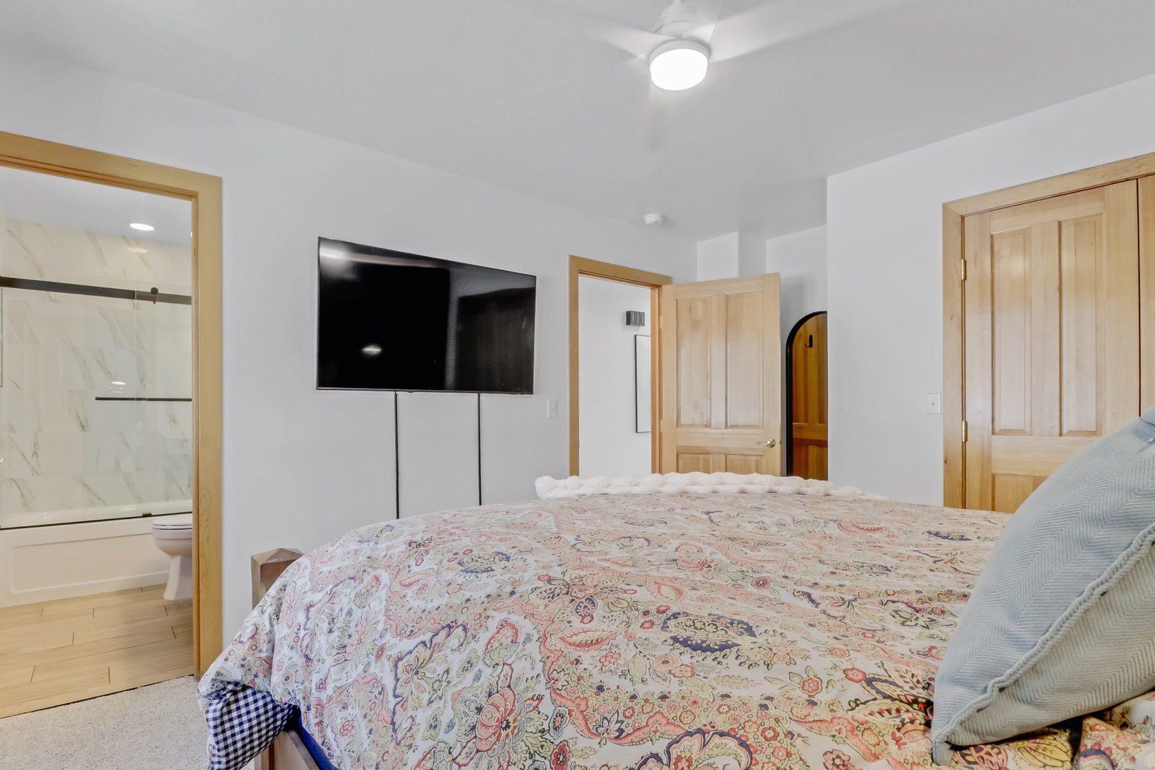 Your master suite features a cozy bed, wall-mounted TV for relaxation, and beautiful natural wood finishes throughout.