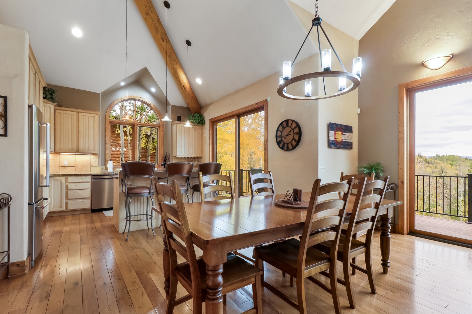 Gather around the farmhouse-style table in this bright, open space where warm wood tones meet soaring ceilings. Enjoy meals with a view as natural light pours through large windows and glass doors, framing fall foliage and distant hills.