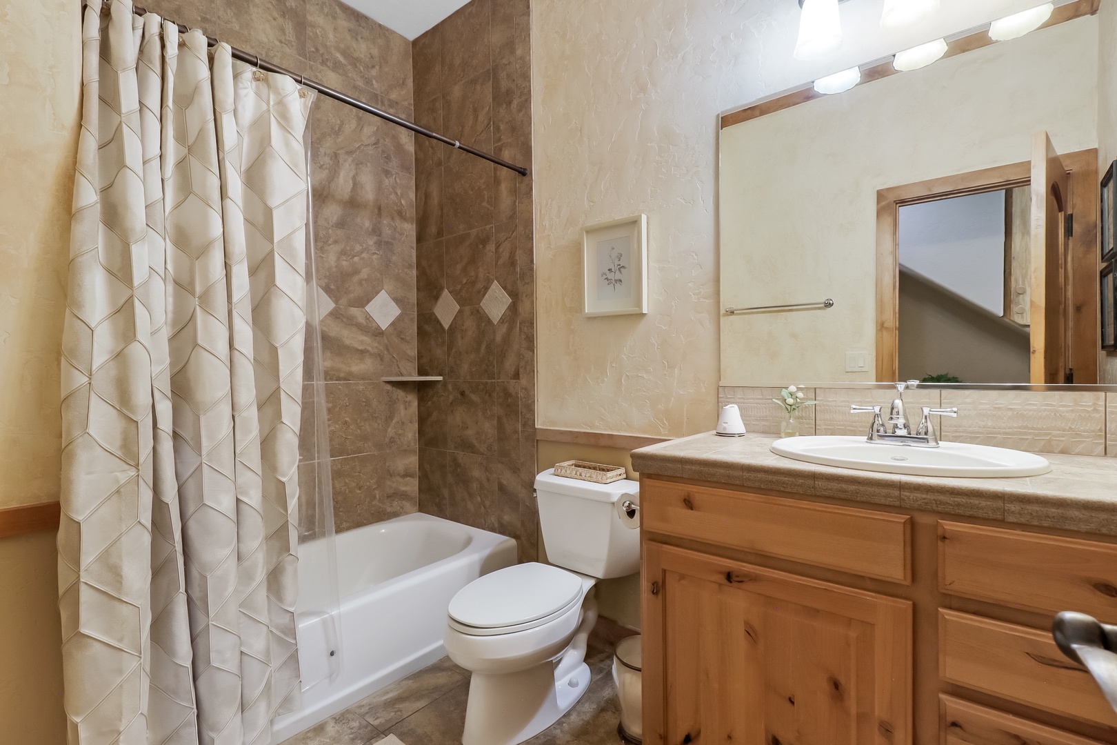 This bathroom offers warm marble tiling and a relaxing tub-shower combo. Enjoy the natural wood vanity, bright vanity lighting, and thoughtful touches like fresh linens waiting for you.