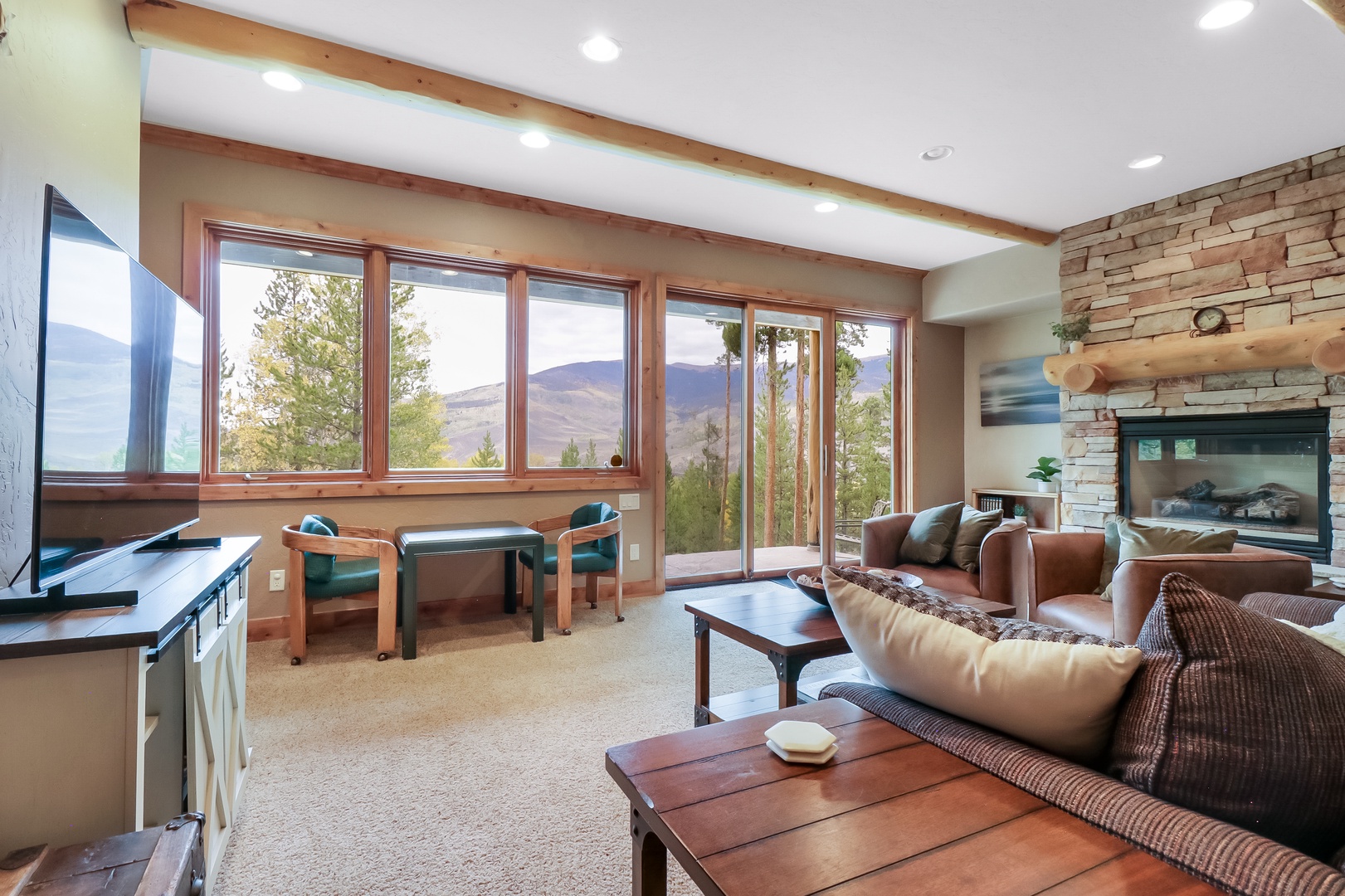 Unwind in your spacious living room, where panoramic windows frame stunning mountain vistas and natural light pours over comfortable seating. The stone fireplace adds warmth while you relax and take in the peaceful surroundings.