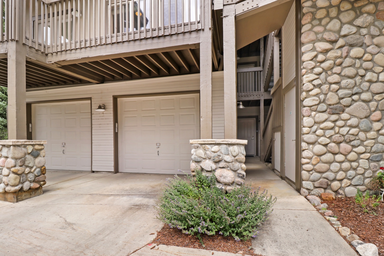 The property features secure garage parking with a welcoming entrance framed by natural stone accents and private balconies above, offering convenient access for your arrival.