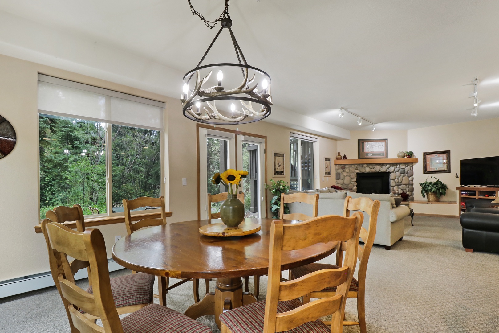 Spacious dining table flooded with natural light overlooking lush greenery, with an adjacent cozy living area and stone fireplace for unwinding.