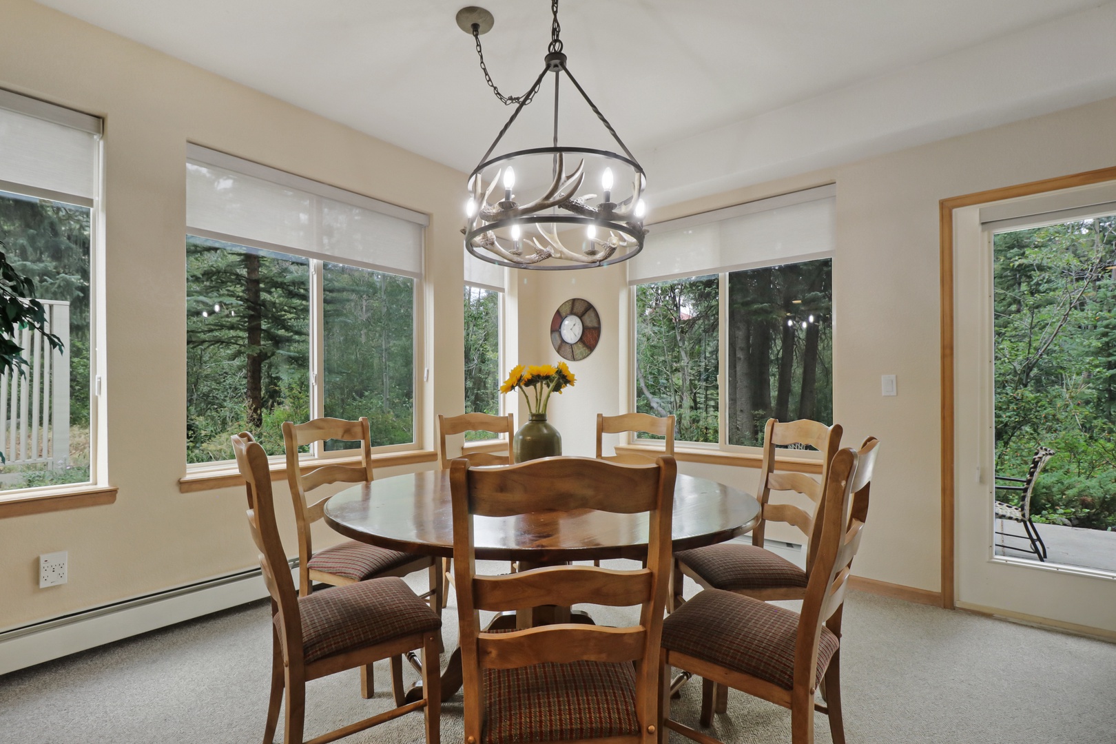 Gather around the beautiful wooden table under a rustic chandelier as natural light pours through windows overlooking lush forest views—perfect for memorable meals together.