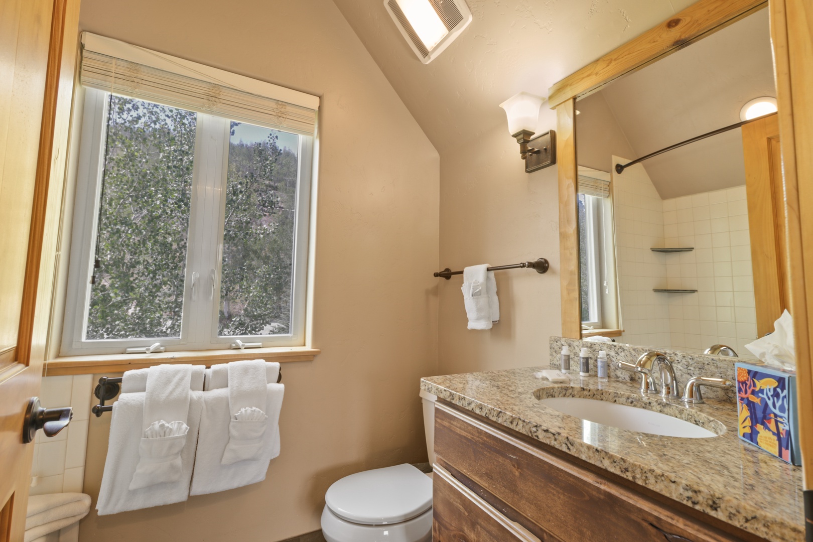 Step into your private spa-like retreat with warm wood tones, a granite vanity, and a bright window framing winter views. Fresh towels await after your refreshing shower.