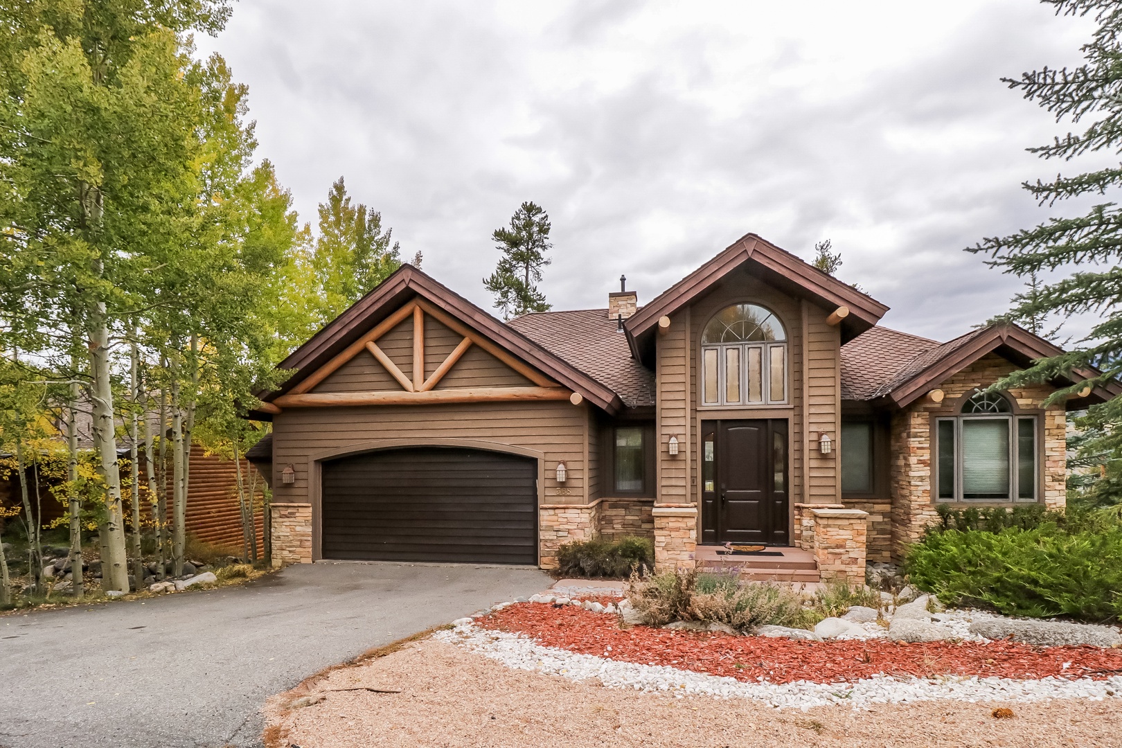 A charming mountain retreat featuring stone and wood details, surrounded by aspens and evergreens. The property offers convenient parking and a welcoming entrance in a serene natural setting.