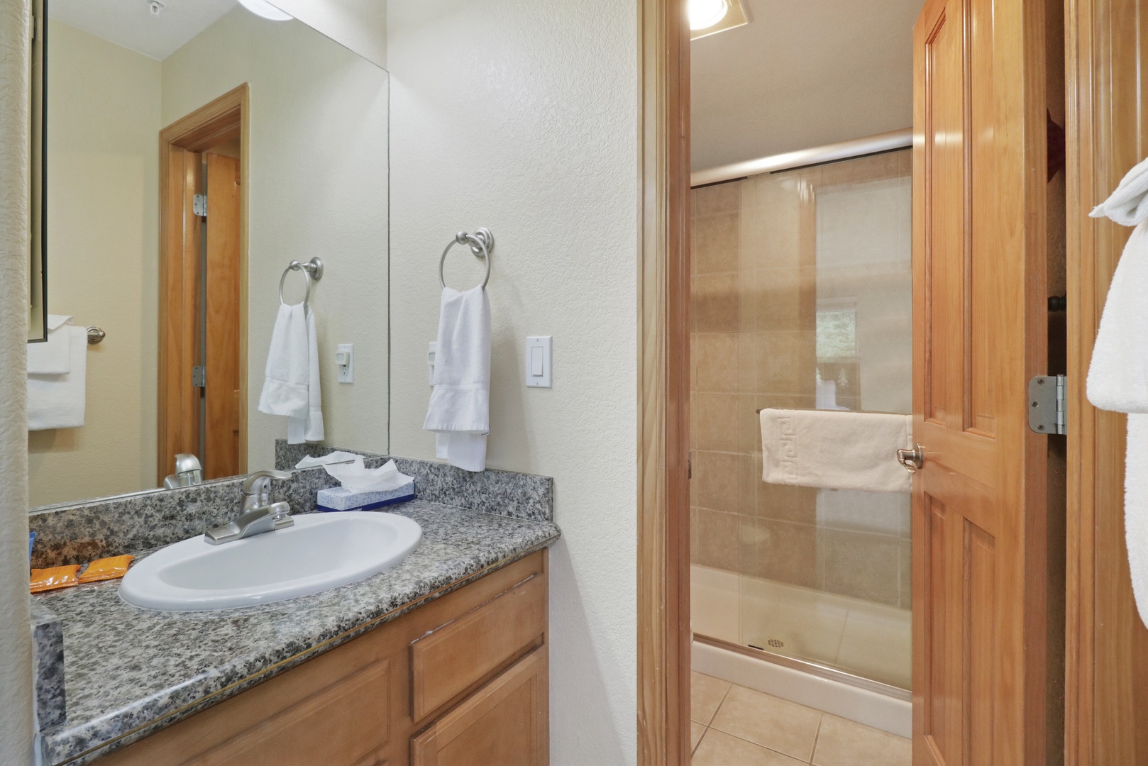 Step into a clean, well-appointed bathroom where crisp towels and granite counters await your arrival, with a convenient glass-enclosed shower ready for your use.