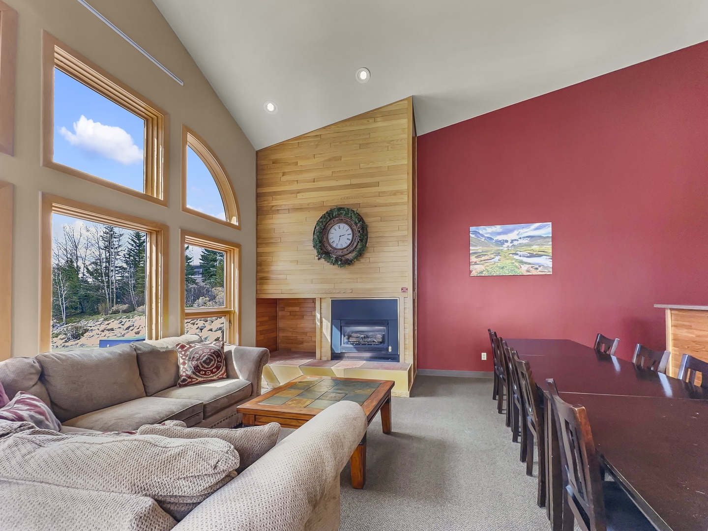 Relax in shared spacious living room with soaring ceilings, cozy fireplace, and stunning mountain views through panoramic windows.