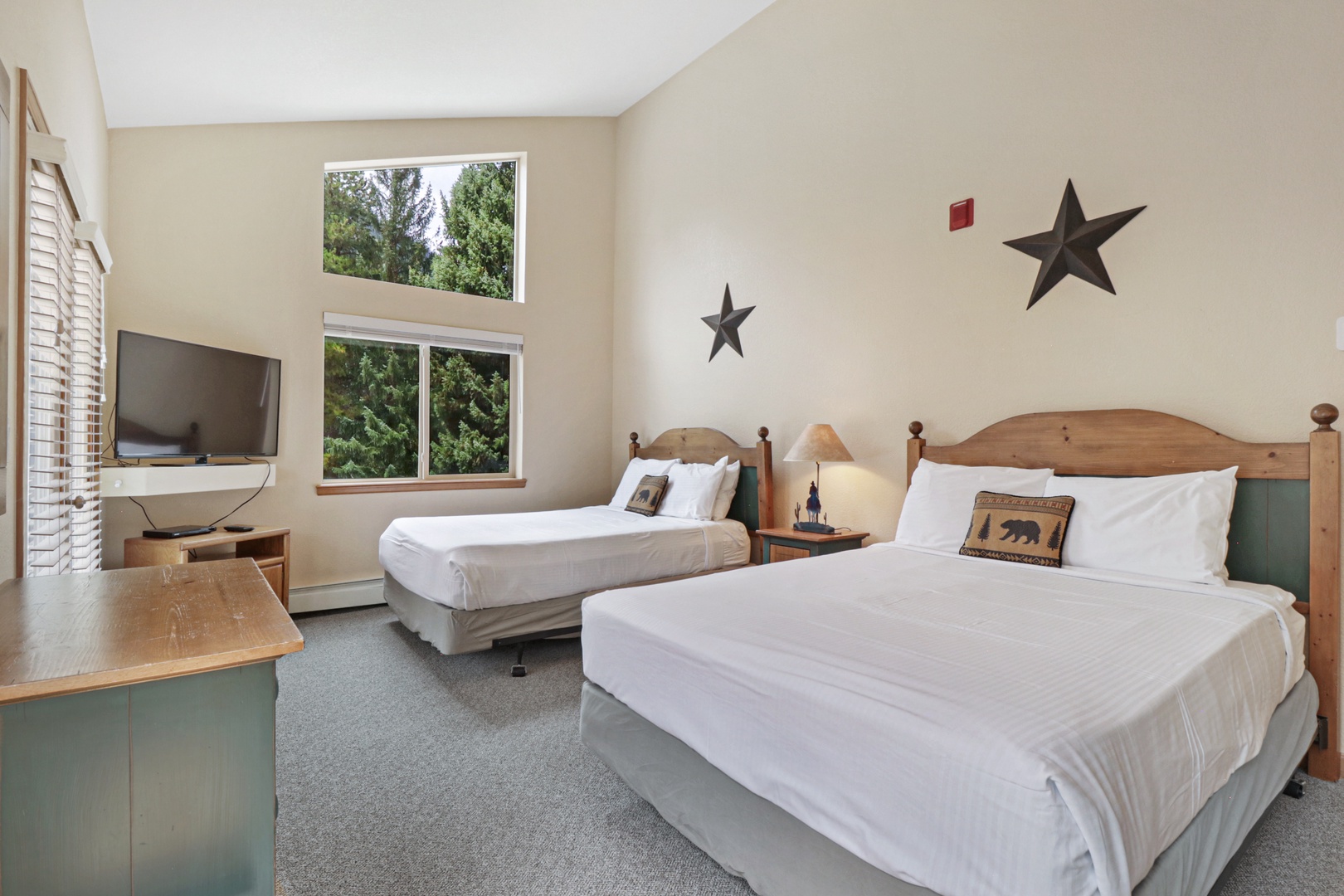Rest easy in your bright, inviting bedroom with two comfortable queen beds, crisp linens, and cheerful natural light streaming through the windows. The rustic wood furnishings and charming star accents create a cozy, welcoming retreat for your stay.