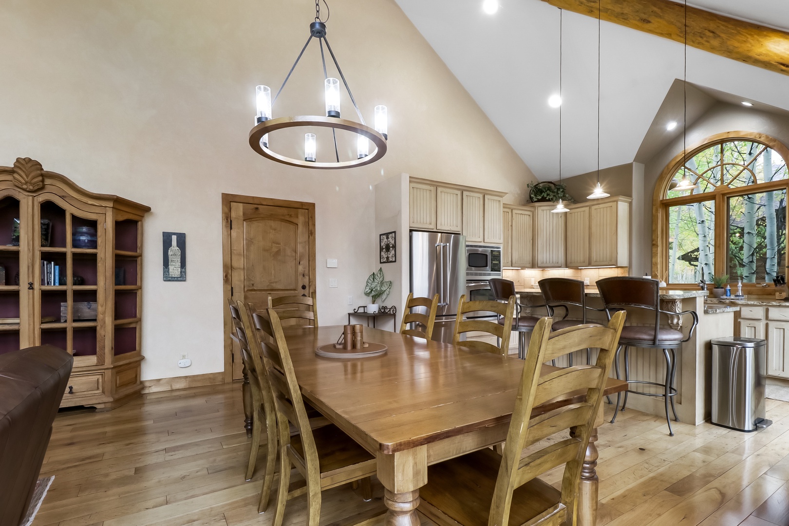 Gather around this beautiful wooden dining table under vaulted ceilings and rustic chandeliers. The open layout flows into a fully equipped kitchen with natural light and arched windows, perfect for meals and memories.