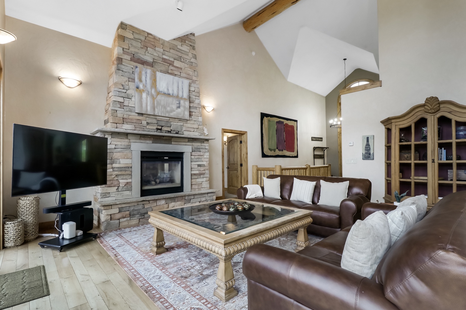 Sink into plush leather sofas and warm up by the stone fireplace in your spacious living room, where soaring ceilings and rustic wood beams create a cozy mountain retreat.