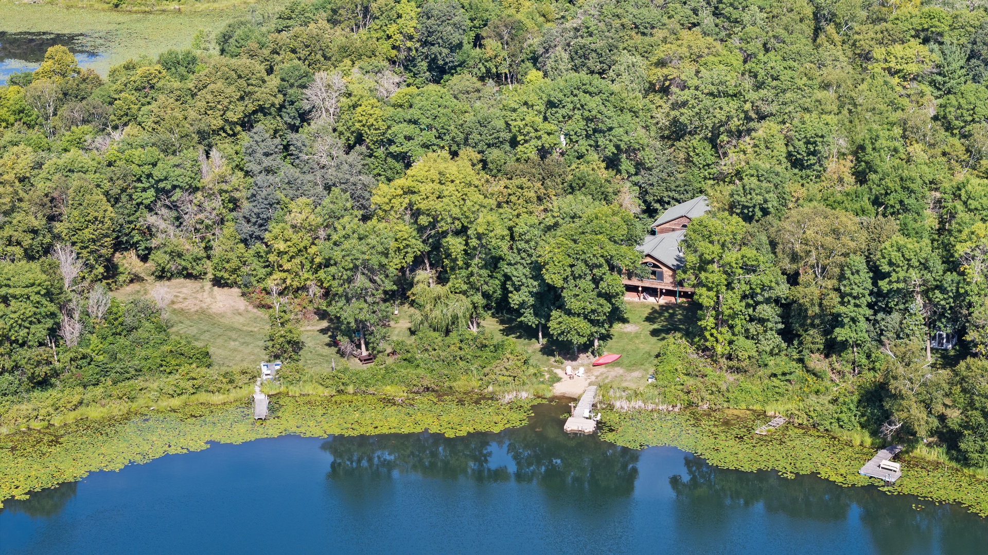 Aerial view of the lakeside property nestled among lush greenery with private waterfront access and dock.