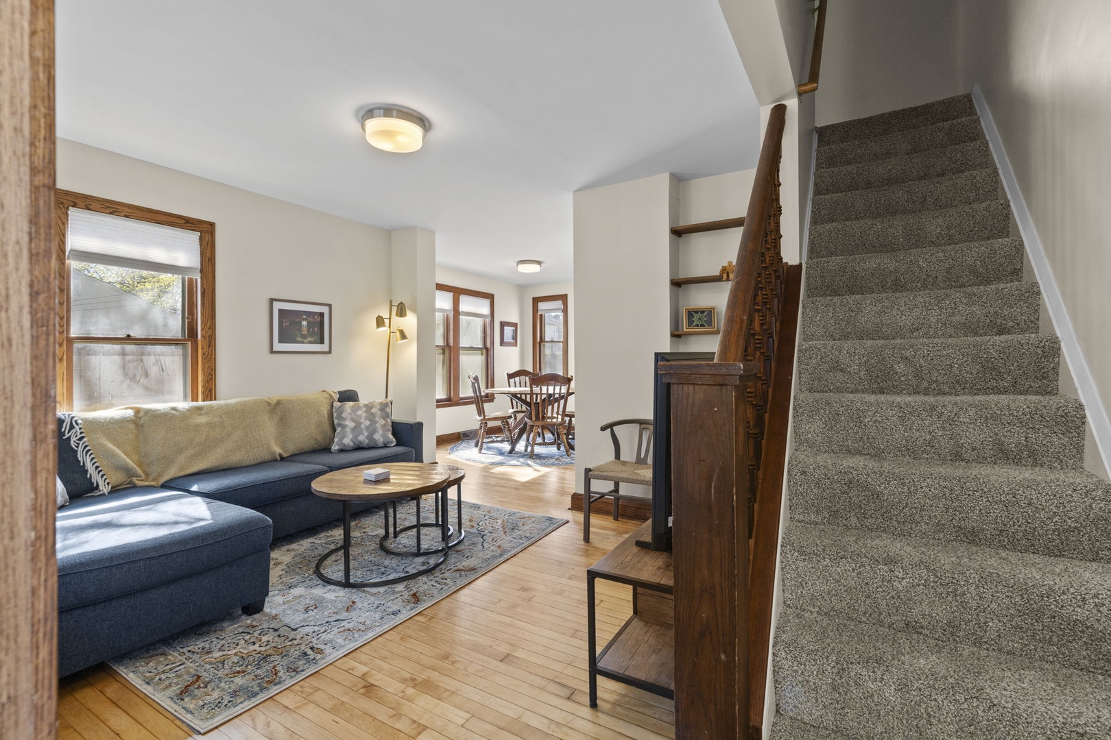 Overhead view of the open living and dining area — hardwood floors, sectional sofa, and natural light pour through original wood-framed windows.