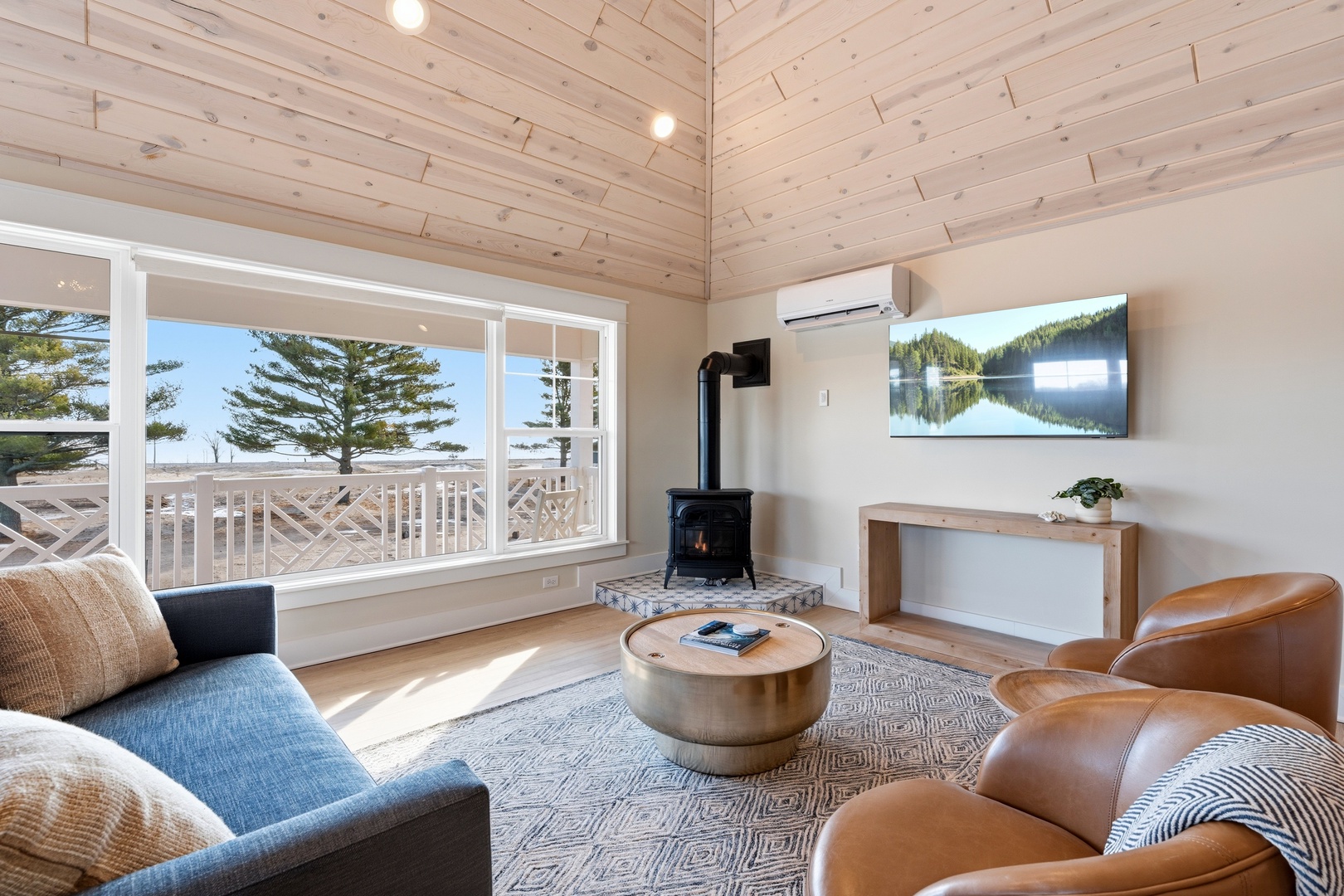 Relax in this sun-drenched coastal retreat, where exposed wood ceilings and a cozy fireplace create a warm sanctuary, and expansive windows frame beachside pines just steps away.