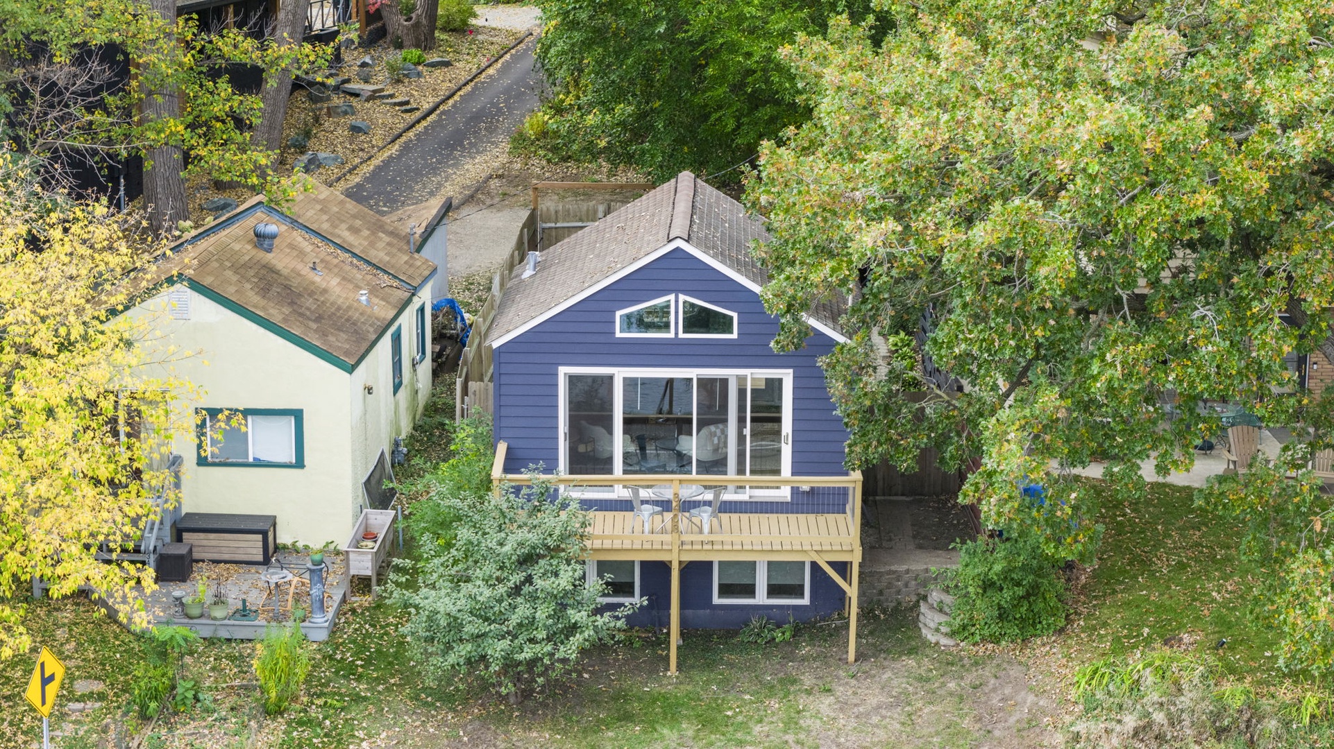 This charming property features a distinctive blue cottage surrounded by mature trees and greenery, offering a peaceful retreat with spacious outdoor areas and a welcoming deck for relaxation.