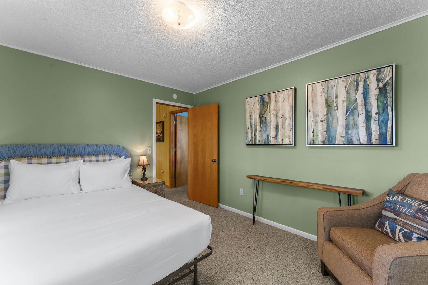 Settle into crisp white linens and let the serene sage walls soothe you. Your peaceful retreat features calming birch tree artwork and a cozy corner chair for unwinding after your adventures.