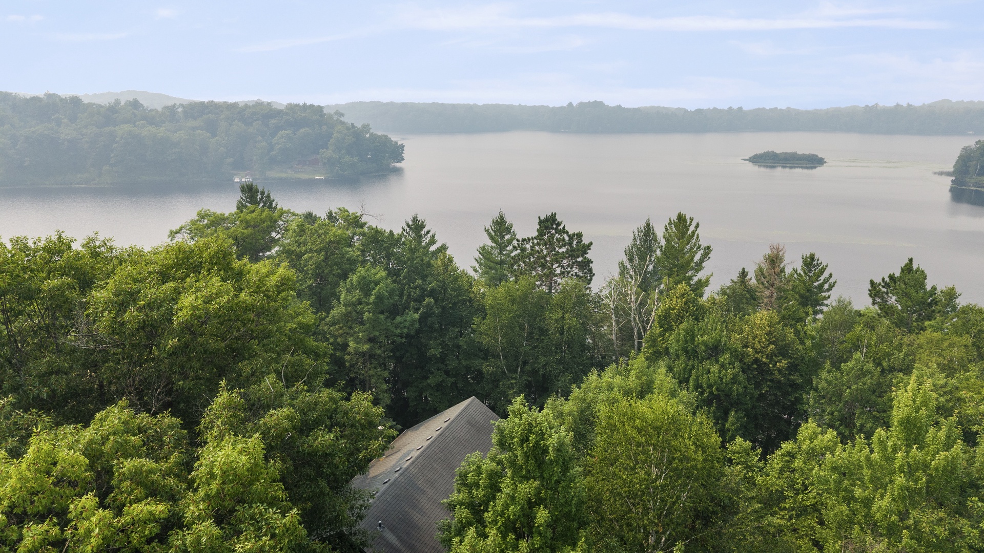 Elevated property view overlooking a serene lake surrounded by lush greenery and gentle hills, nestled in a peaceful natural setting.
