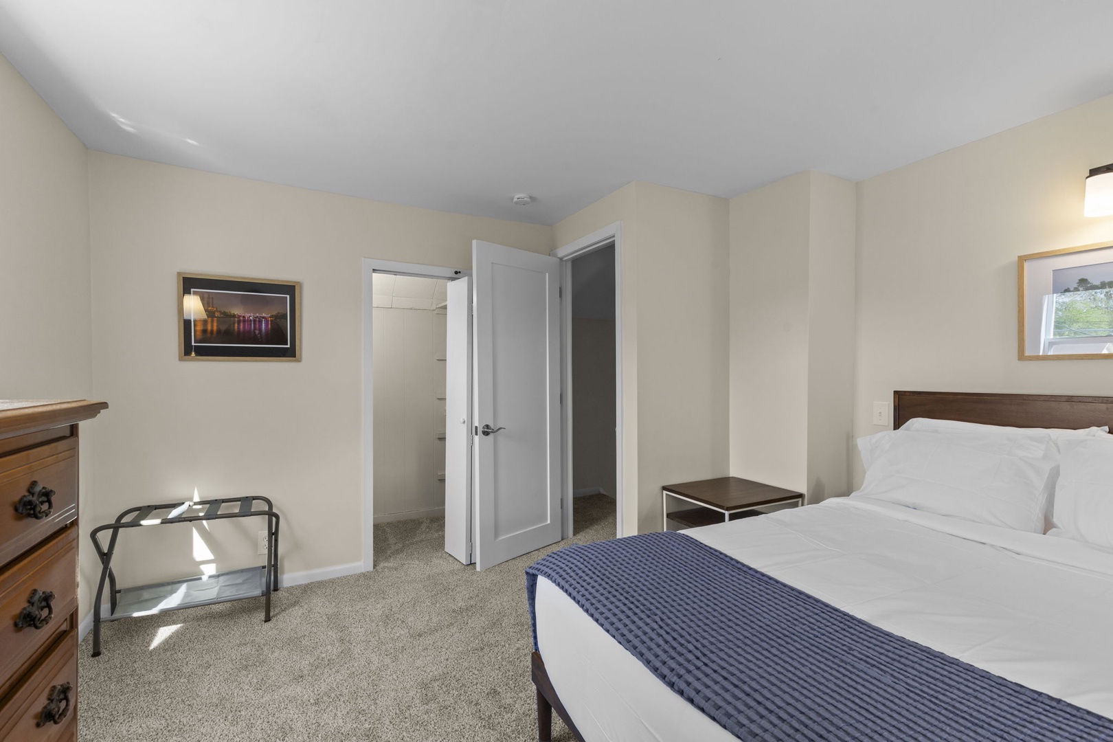 Queen bedroom with luggage rack, tall dresser, and access to a walk-in closet — thoughtfully outfitted for a comfortable stay.