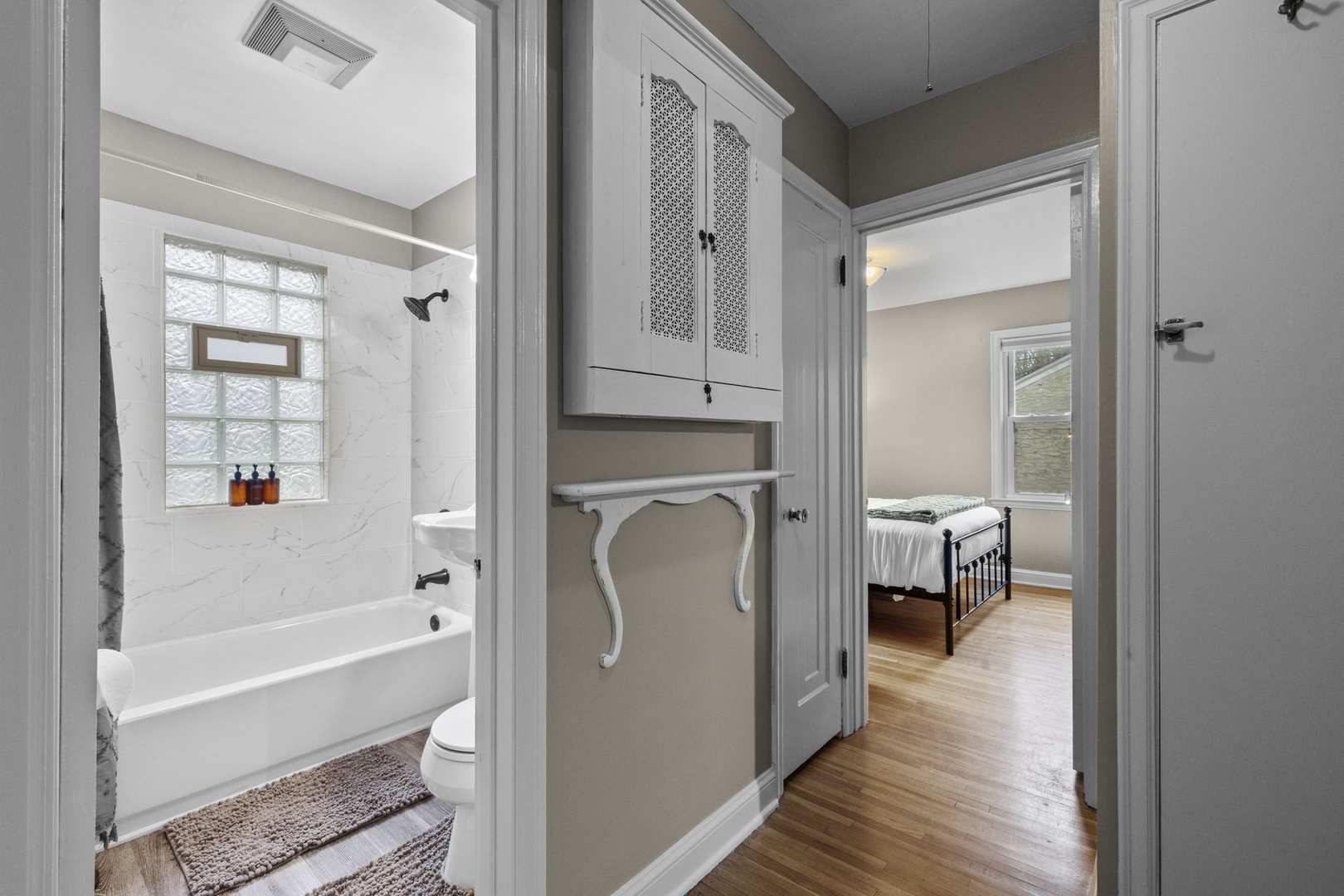 Step into your private hallway connecting a bright bathroom and cozy bedroom, with charming storage details and warm hardwood underfoot.
