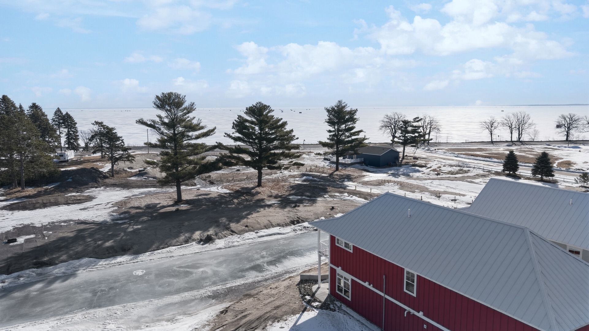 Aerial lakefront view with red house rooftop and frozen bay