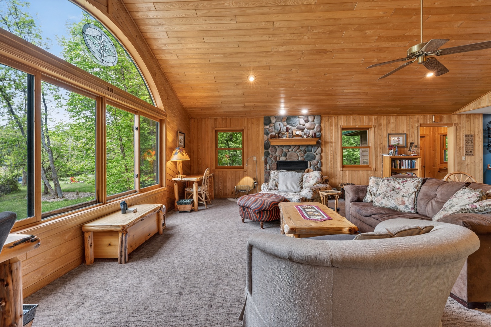 Unwind in your spacious living room with soaring wood ceilings, a stunning stone fireplace, and large windows framing lush trees and lake views. Plush seating and cozy lighting invite you to relax in complete comfort.