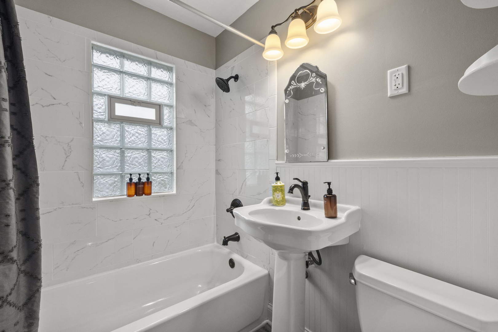 Sleek marble-look tile and warm ambient lighting create your peaceful retreat. Unwind in the tub after exploring, then refresh at the pedestal sink.