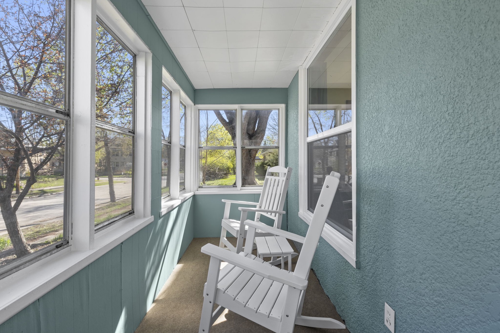 Charming enclosed sunporch with panoramic windows and white rocking chairs — sip your morning coffee and watch the neighborhood come alive.