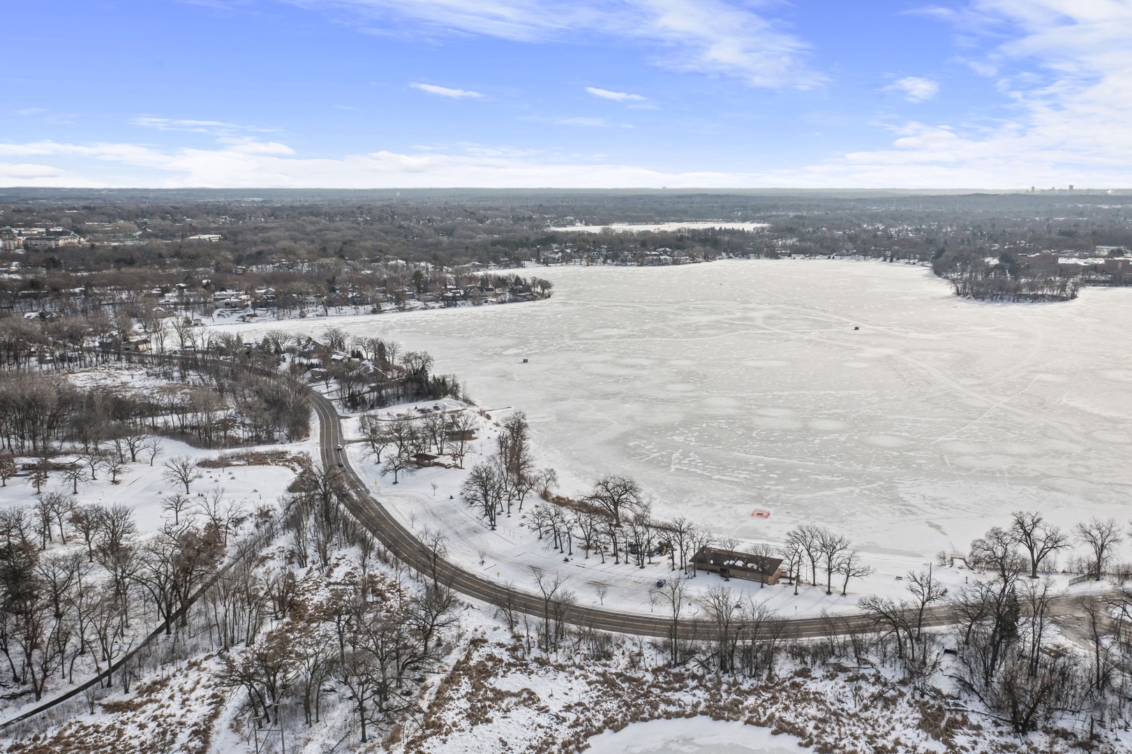 Aerial winter view of frozen lake surrounded by snow-covered residential neighborhoods and winding roads.