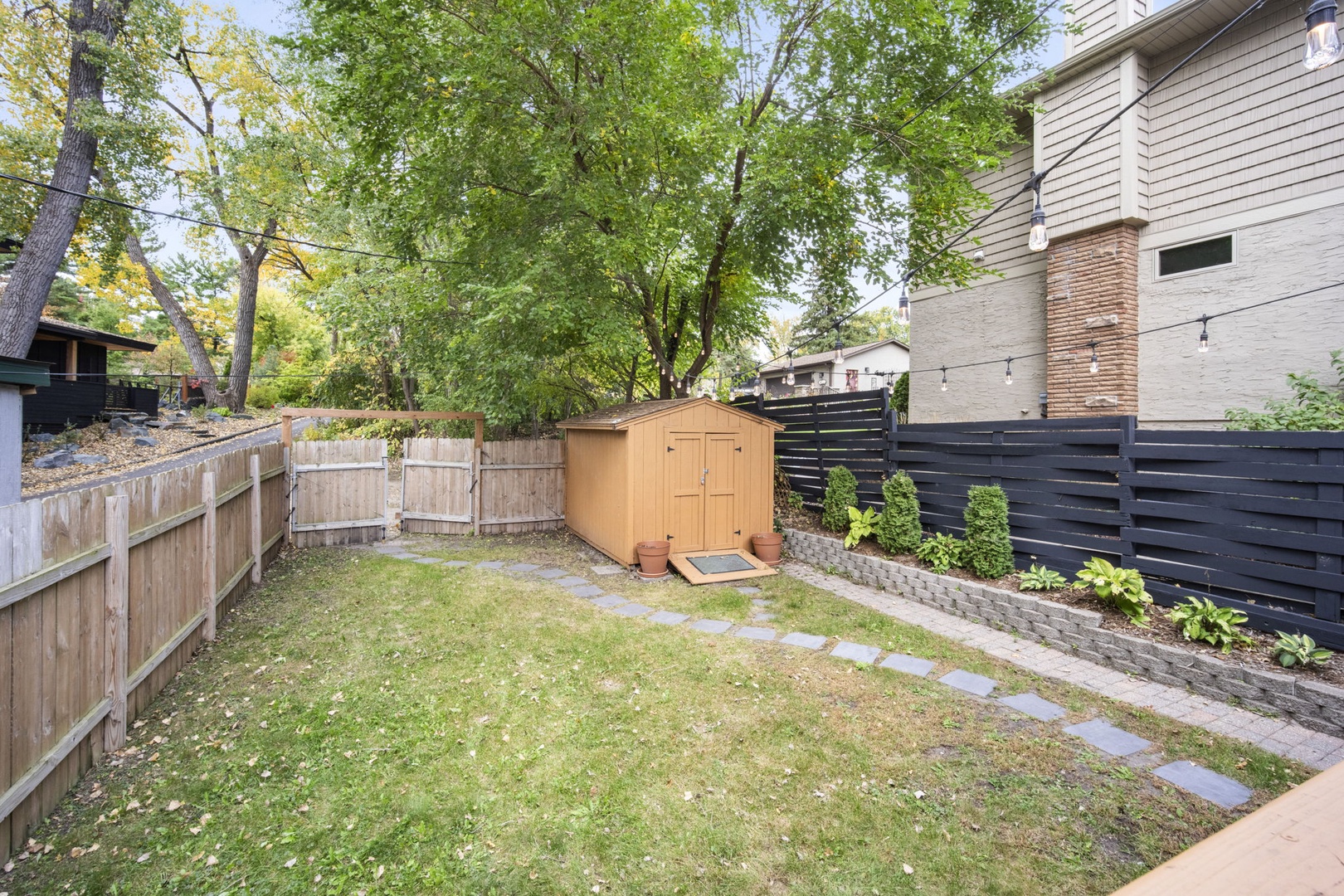 A private backyard awaits, bordered by wooden fencing and lush trees, with a storage shed and stepping-stone path through the grass.