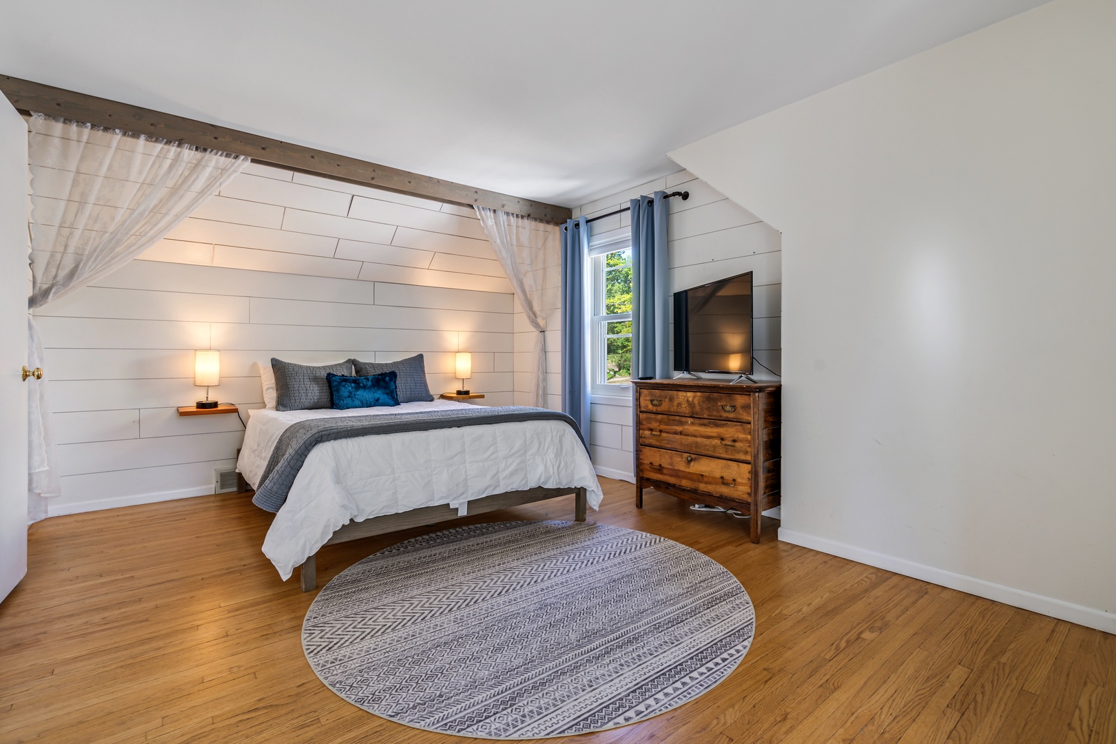 24 — Queen Bedroom Summer View with Shiplap Wall Warm Lighting and Hardwood Floors