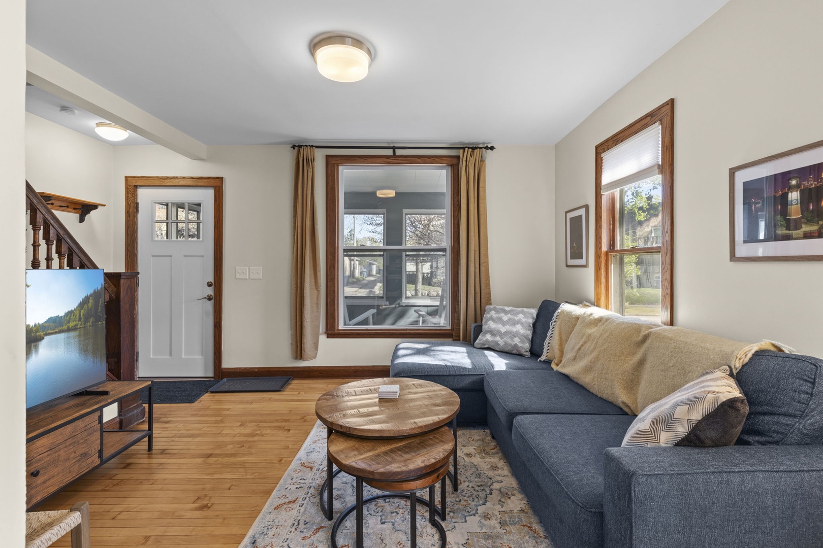 Welcoming living room with L-shaped sectional, large smart TV, and front entry — original staircase with classic wood banister adds timeless Minneapolis character.