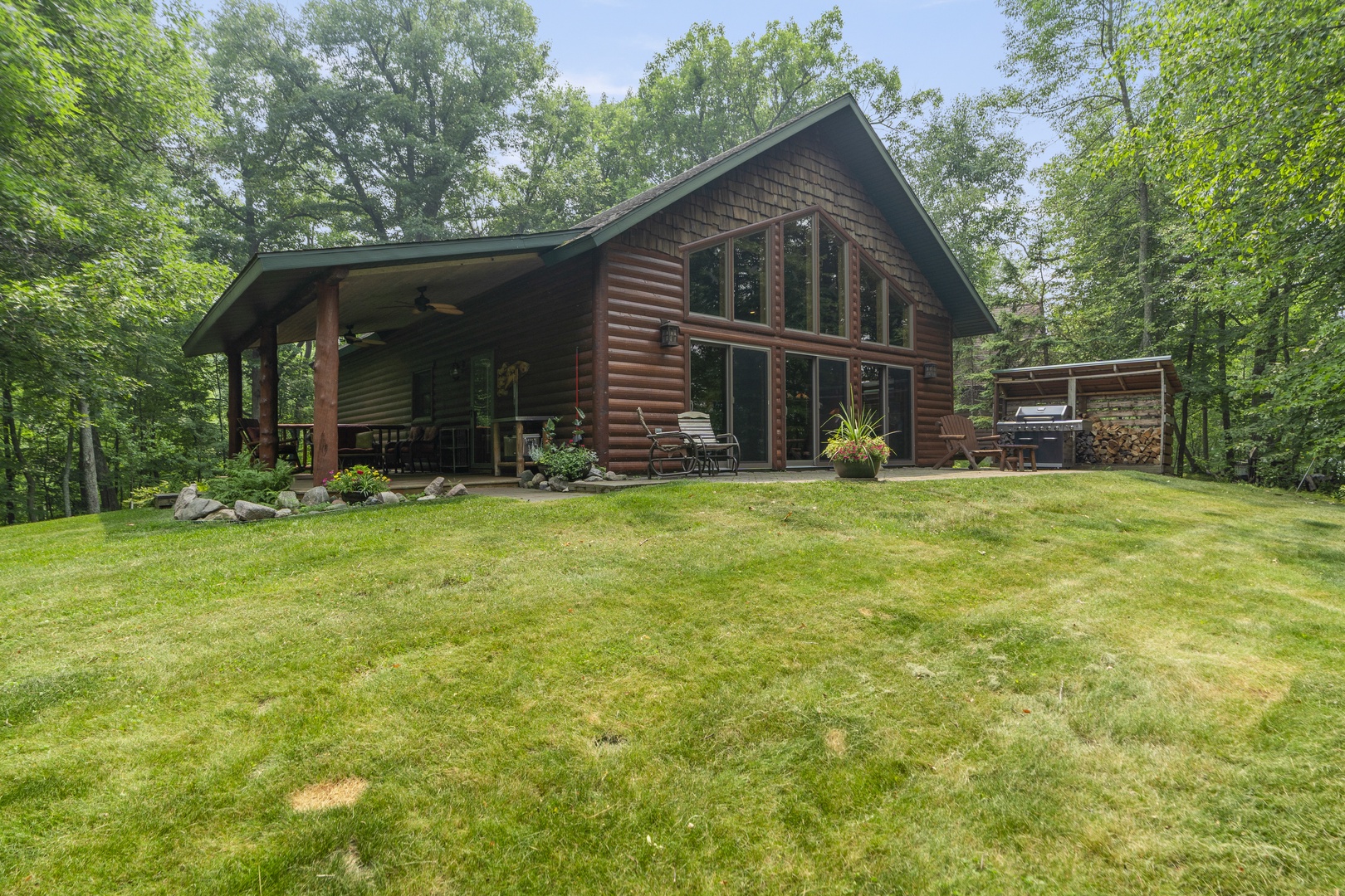 This rustic log cabin sits nestled among towering trees on a spacious private lawn, offering a peaceful woodland retreat with a covered porch and inviting outdoor spaces to unwind.