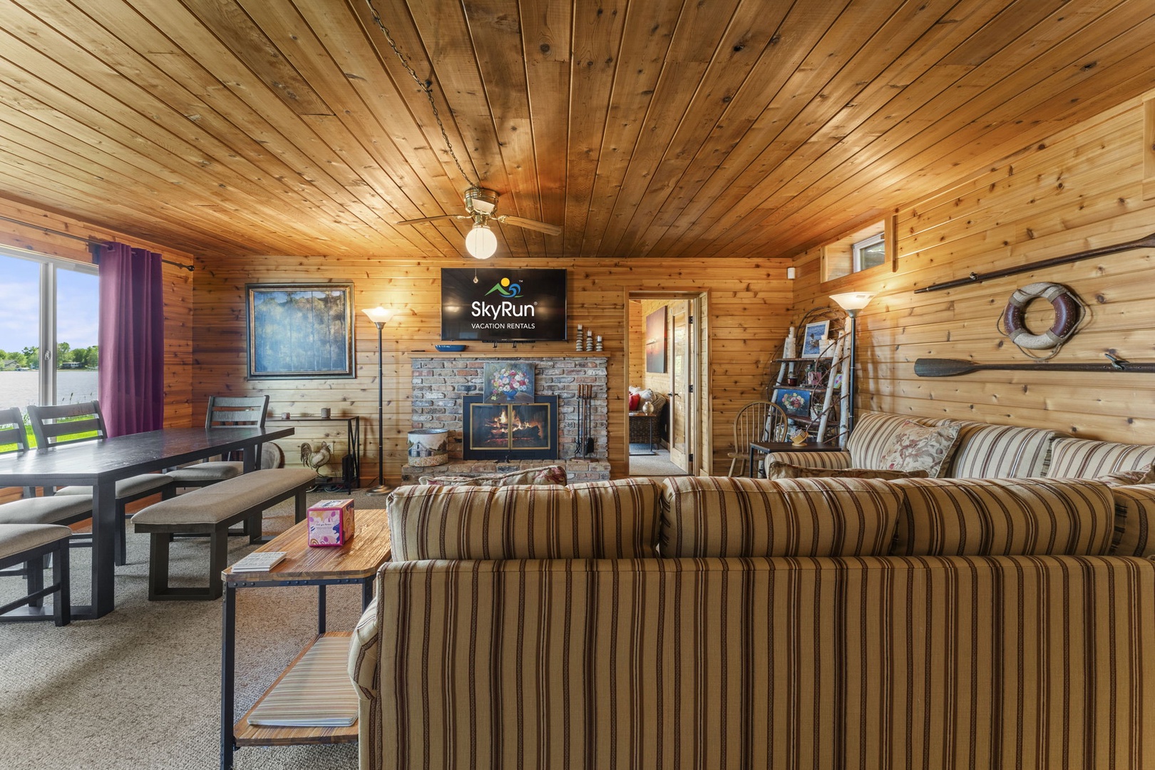 Unwind in this cozy living room with rustic wood paneling, plush seating, and a warm stone fireplace. The open layout and natural light create a welcoming retreat for your stay.