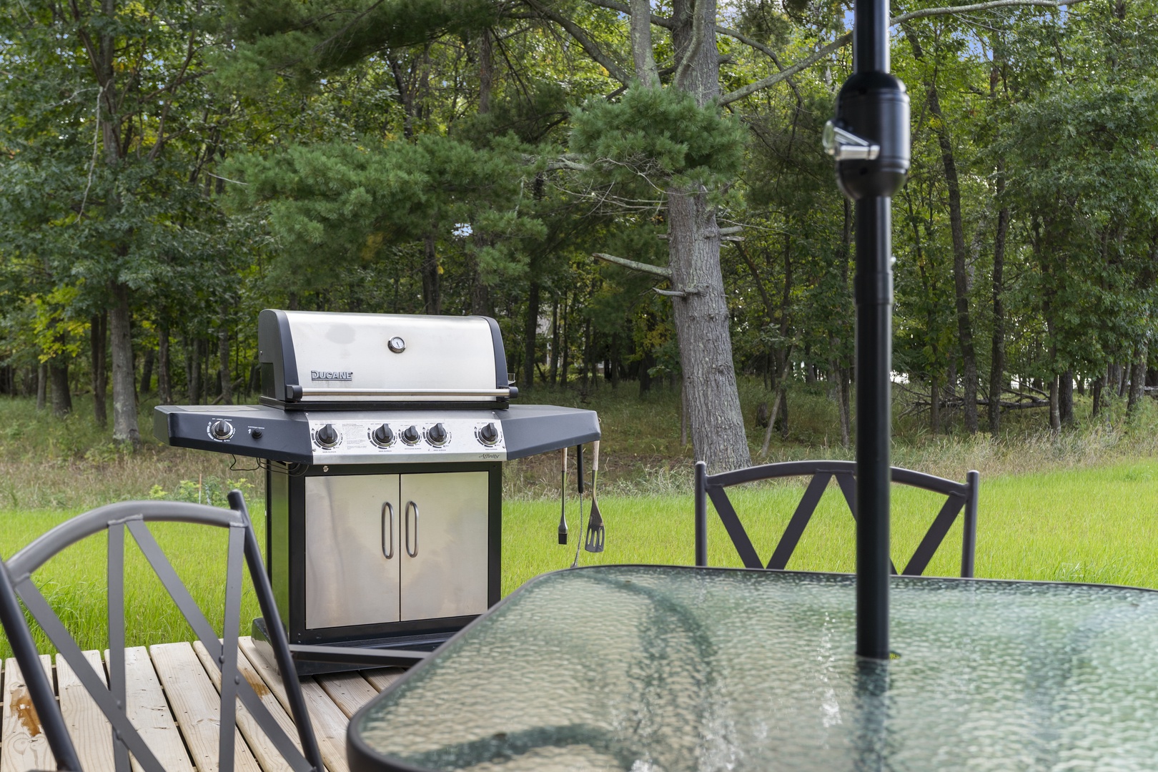 The outdoor deck overlooks a peaceful wooded area, perfect for dining under open skies or grilling your favorite meal on the stainless steel BBQ.