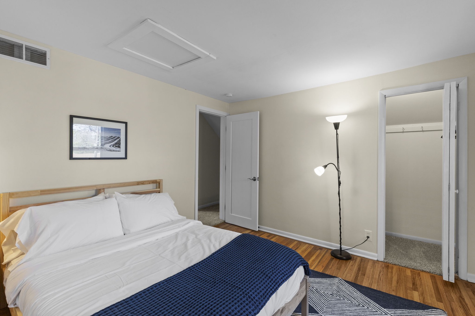 Spacious second bedroom with queen bed, walk-in closet, floor lamp, and hardwood floors — plenty of room to unpack and settle in.