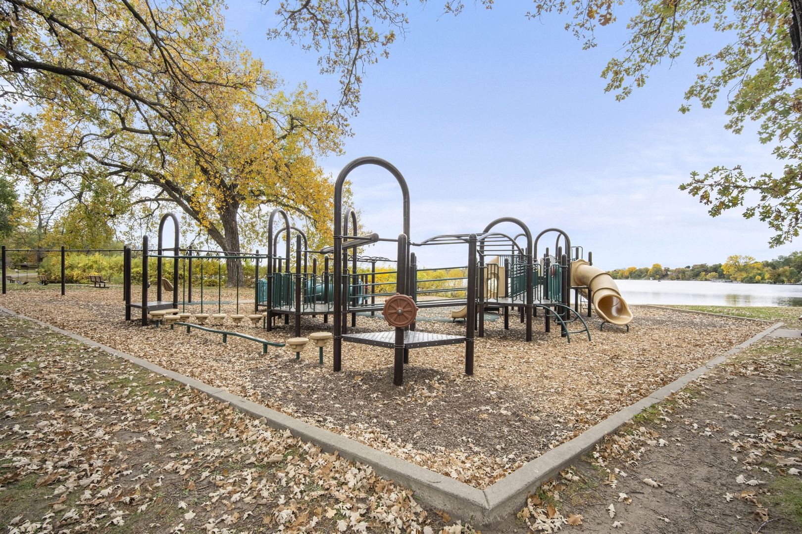 A well-equipped playground beside a peaceful lake, framed by autumn foliage—perfect for families looking to explore the neighborhood's outdoor recreation and natural beauty.