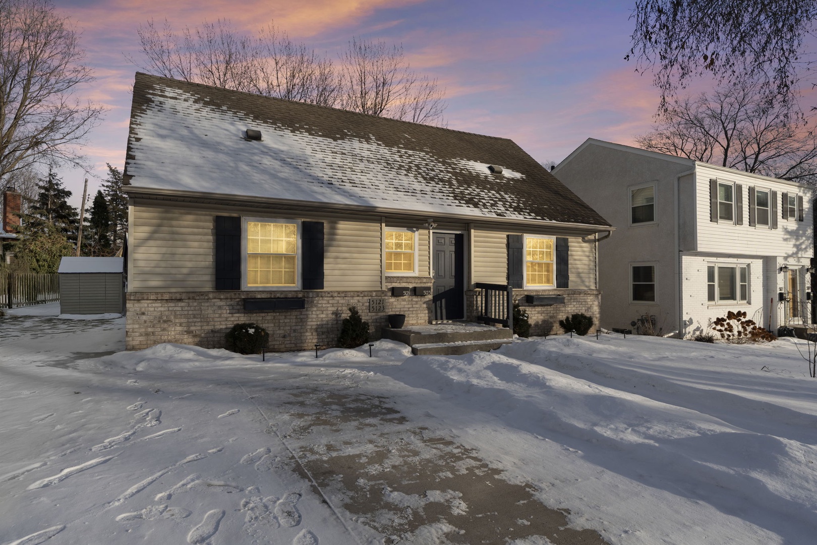 Charming winter retreat with warm, glowing windows and snow-covered grounds in peaceful neighborhood setting.