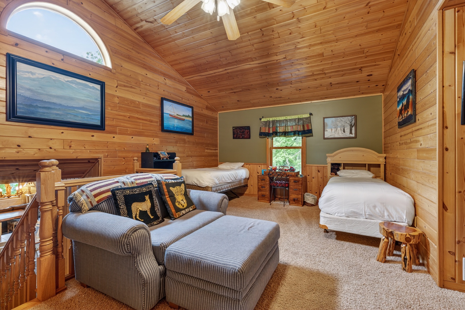 Cozy cabin sleeping loft with pine walls and vaulted ceilings, featuring two comfortable beds and a plush seating area where you can unwind after a day of adventure.