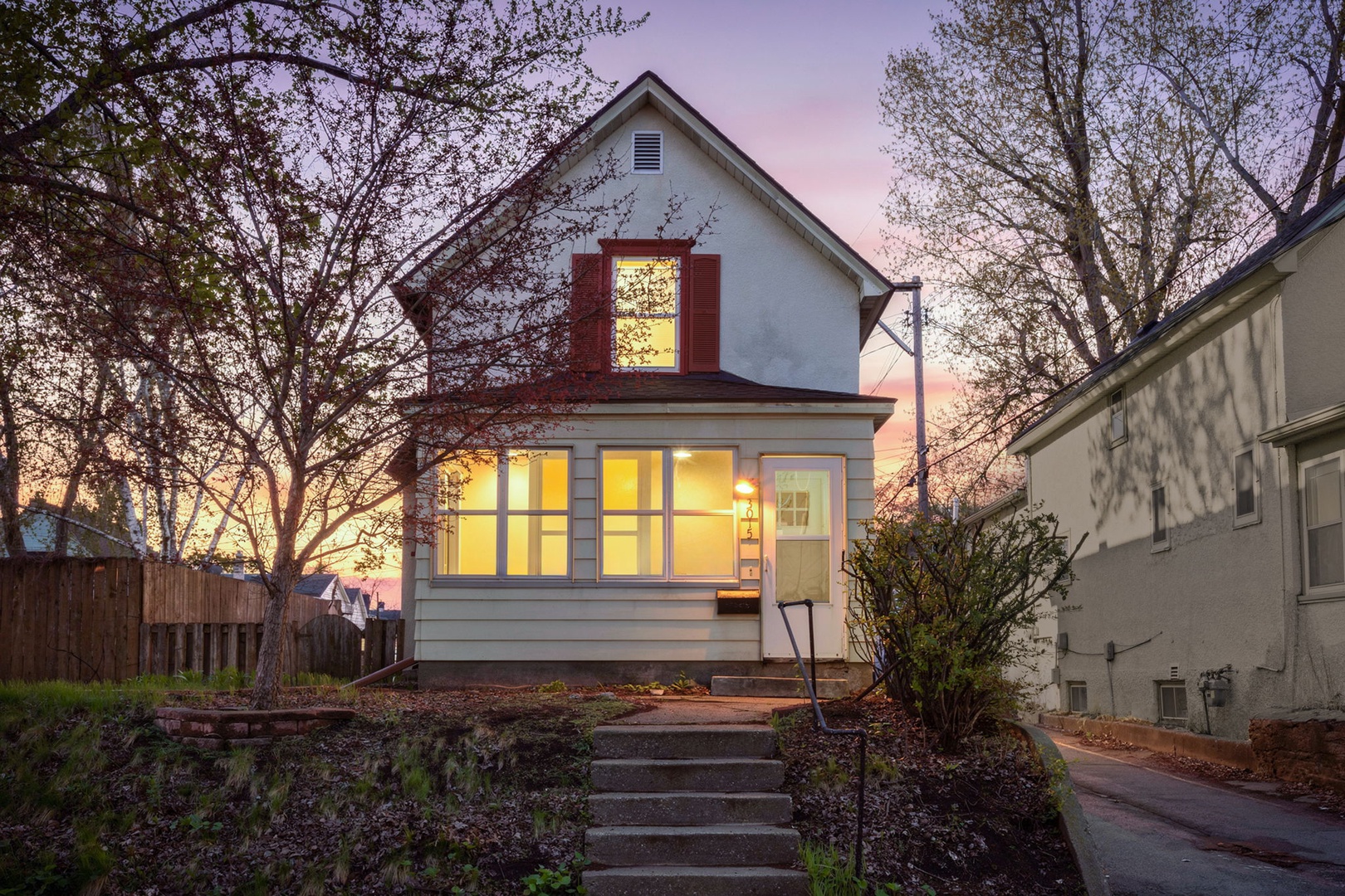 Classic Minneapolis home at golden hour — glowing sunporch, charming curb appeal, and a welcoming front entry in the heart of the city.