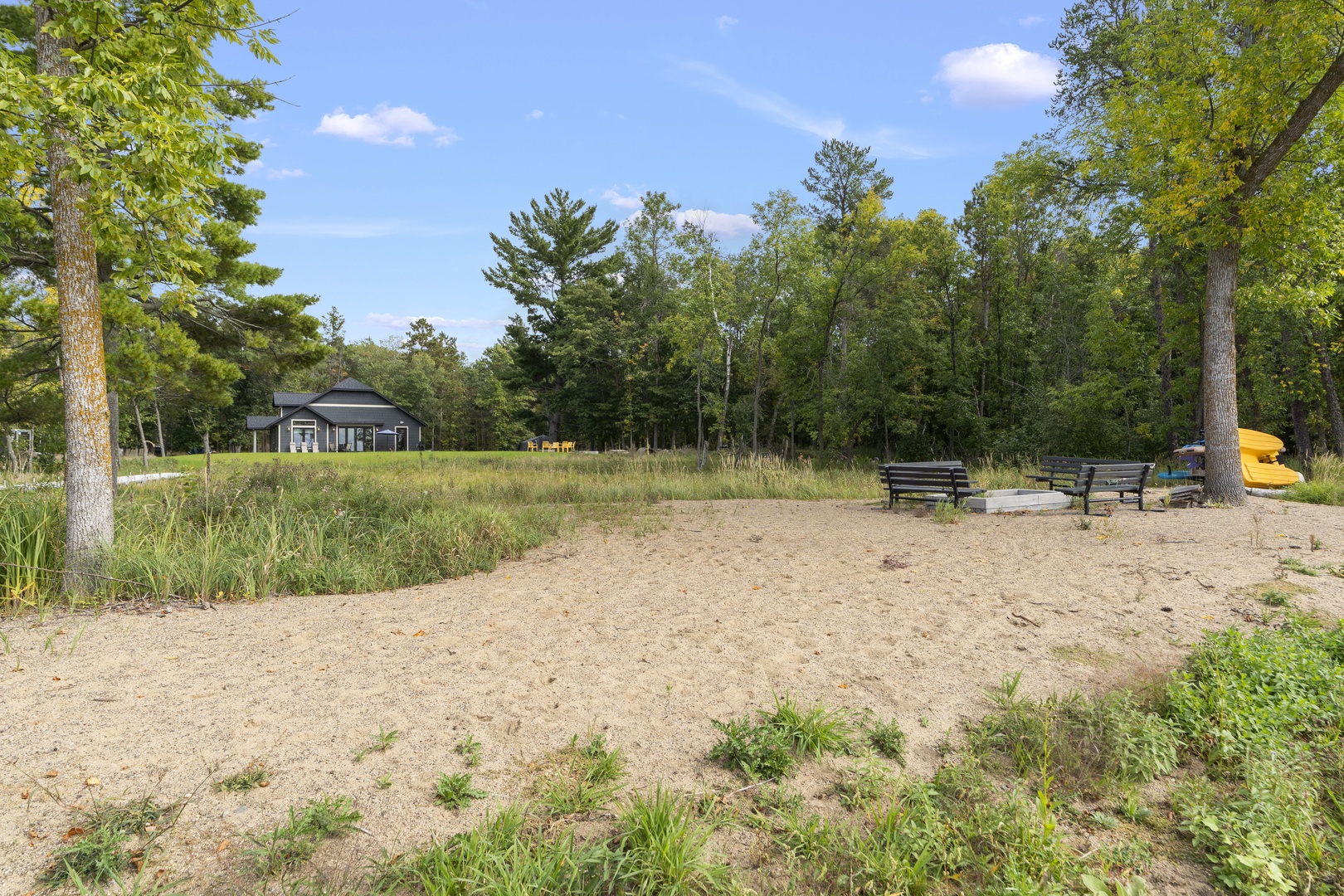 The property features a private sandy beach area surrounded by towering trees and lush natural landscape, with the rental home nestled peacefully in the background.