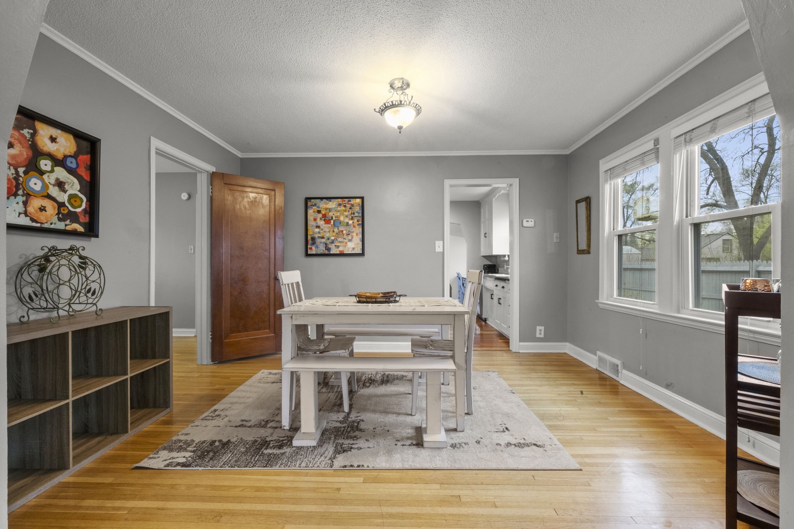 Your dining area features warm wood floors, stylish gray walls, and a farmhouse-style table where you'll gather for meals. Natural light pours in through large windows overlooking the neighborhood.