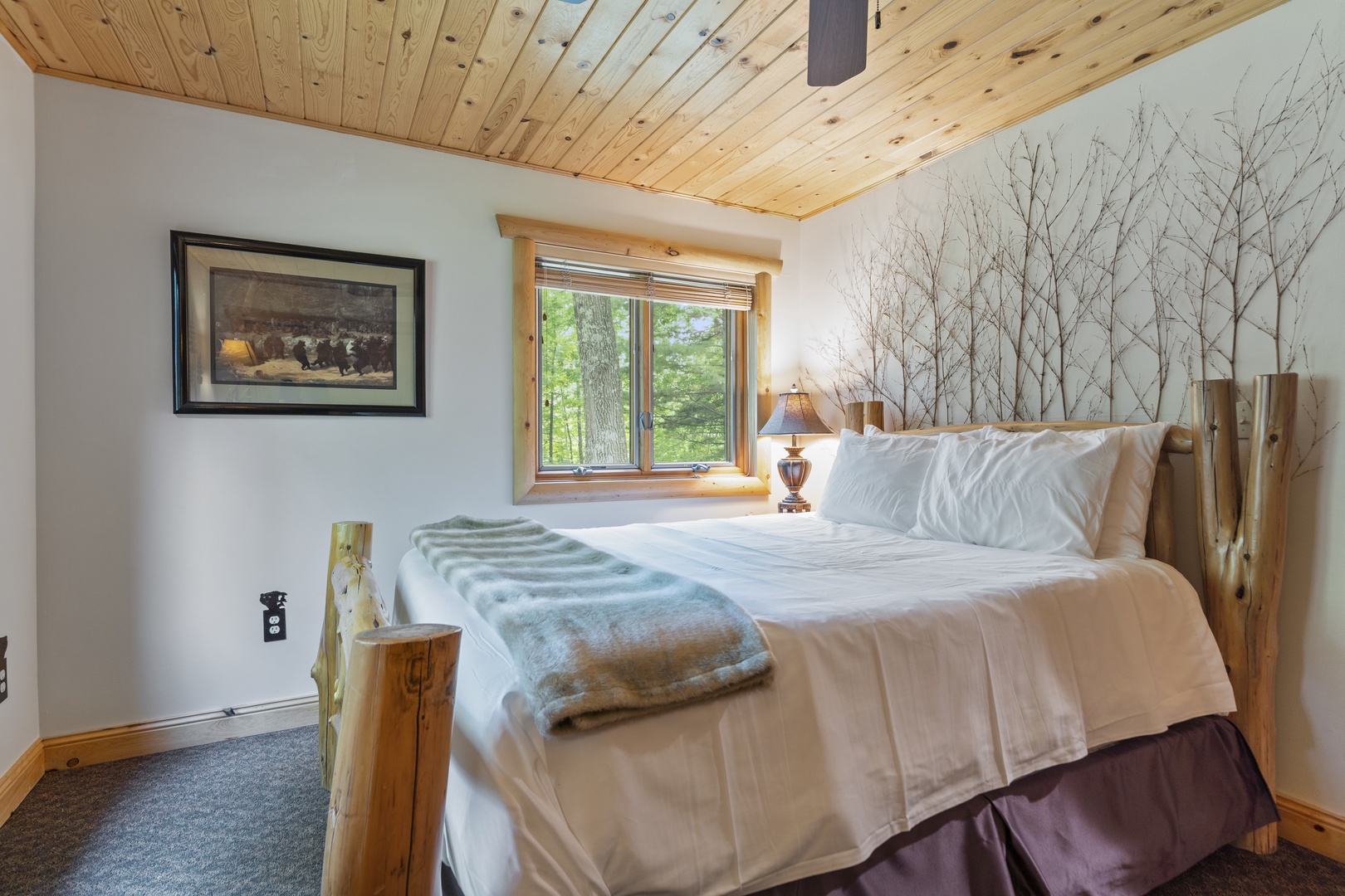 Drift off in this cozy bedroom featuring rustic wood details and crisp linens. Natural light streams through your window, framing a serene forest view that invites peaceful mornings.