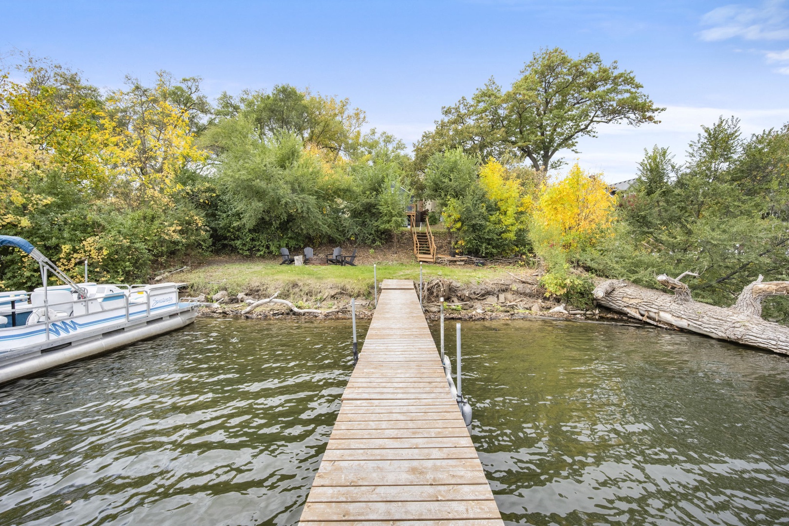 Private dock stretches across tranquil waters to a lush autumn landscape, perfect for lakeside relaxation and water activities.