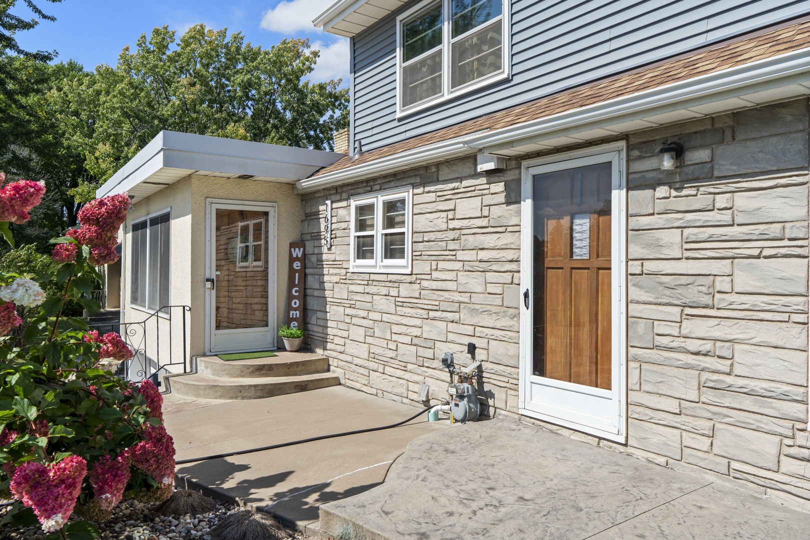 Stone facade entrance with welcoming wooden door and colorful garden landscaping creates an inviting arrival experience.