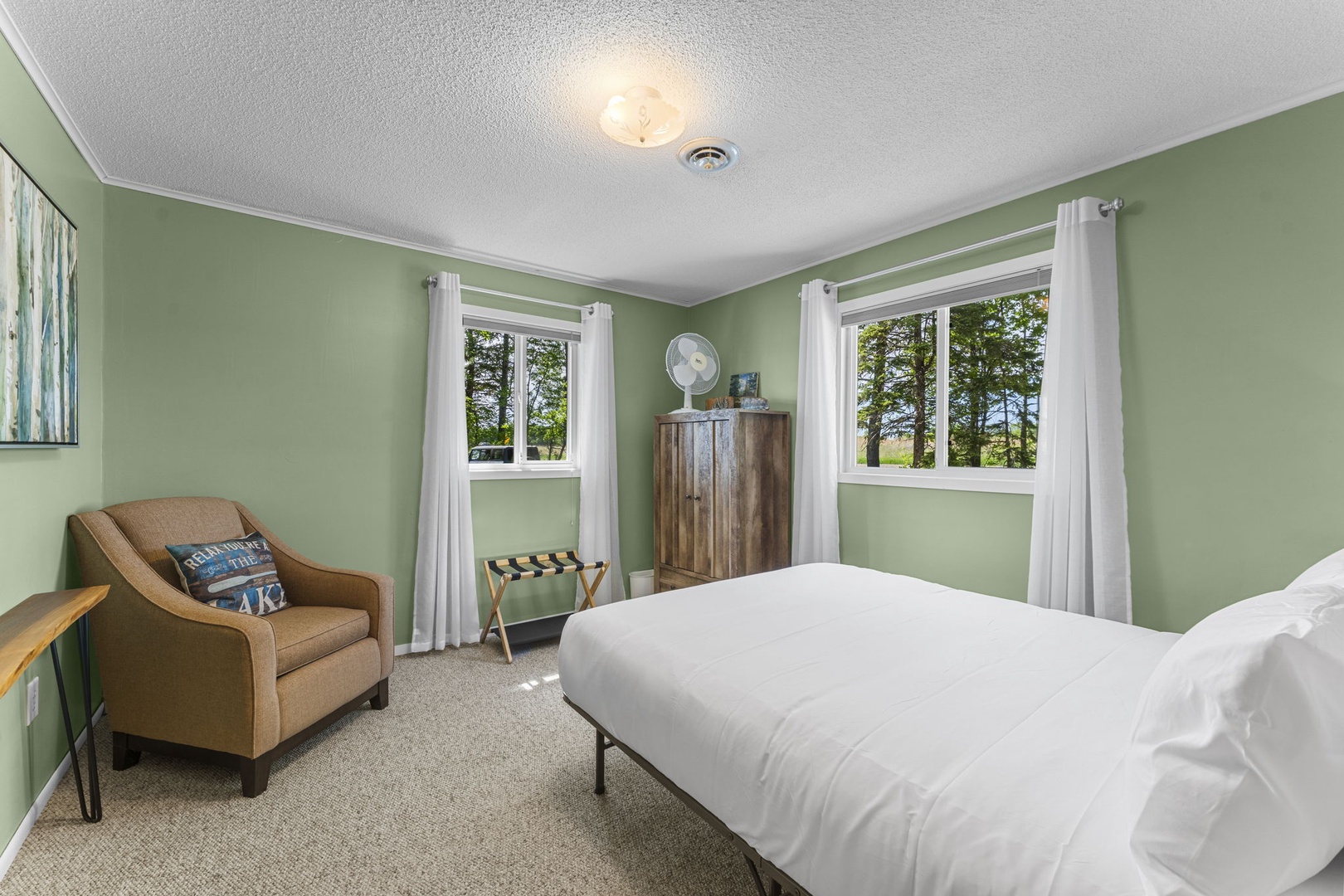 Wake up to serene views of trees and open fields through your windows, with a cozy chair and rustic wardrobe creating a peaceful, inviting retreat for your stay.