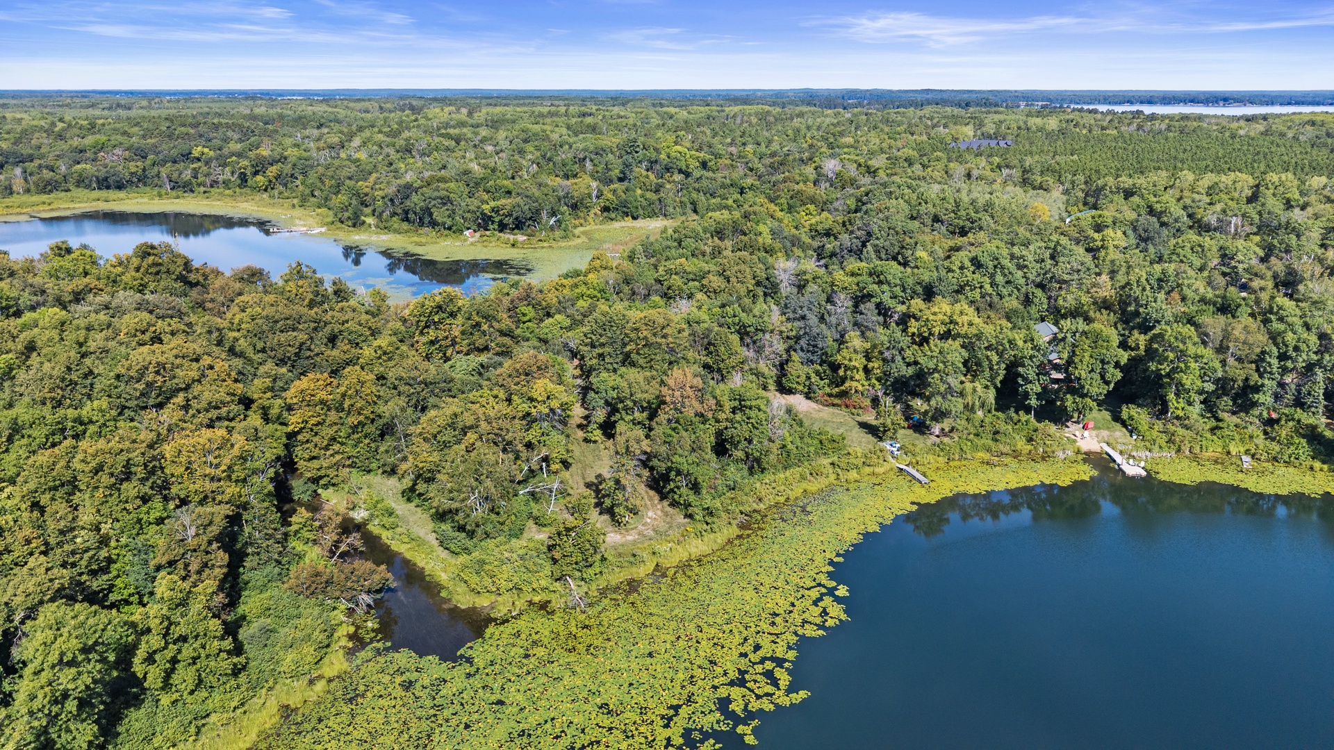 An aerial perspective captures the property's pristine natural setting, nestled among lush forests and tranquil lakefront waters under a bright summer sky.