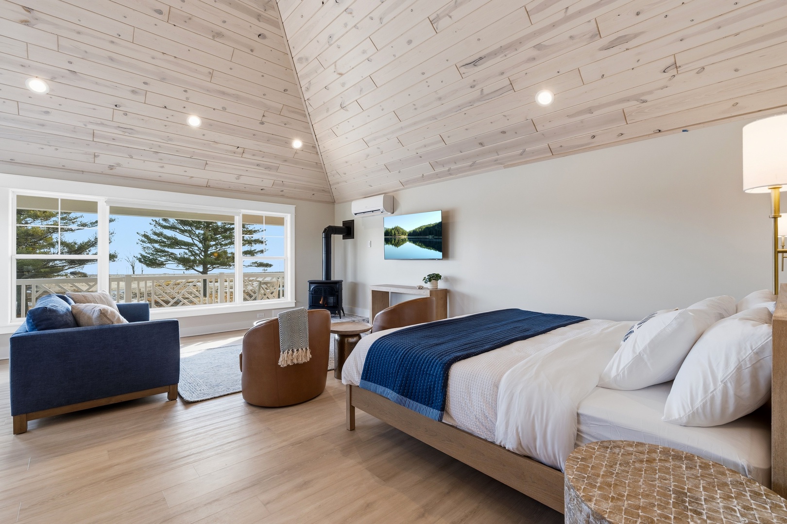 Drift off beneath vaulted wooden ceilings while ocean breezes flow through your spacious coastal bedroom. Wake to sweeping views of pine-dotted shores and endless blue horizon—your private sanctuary by the sea.