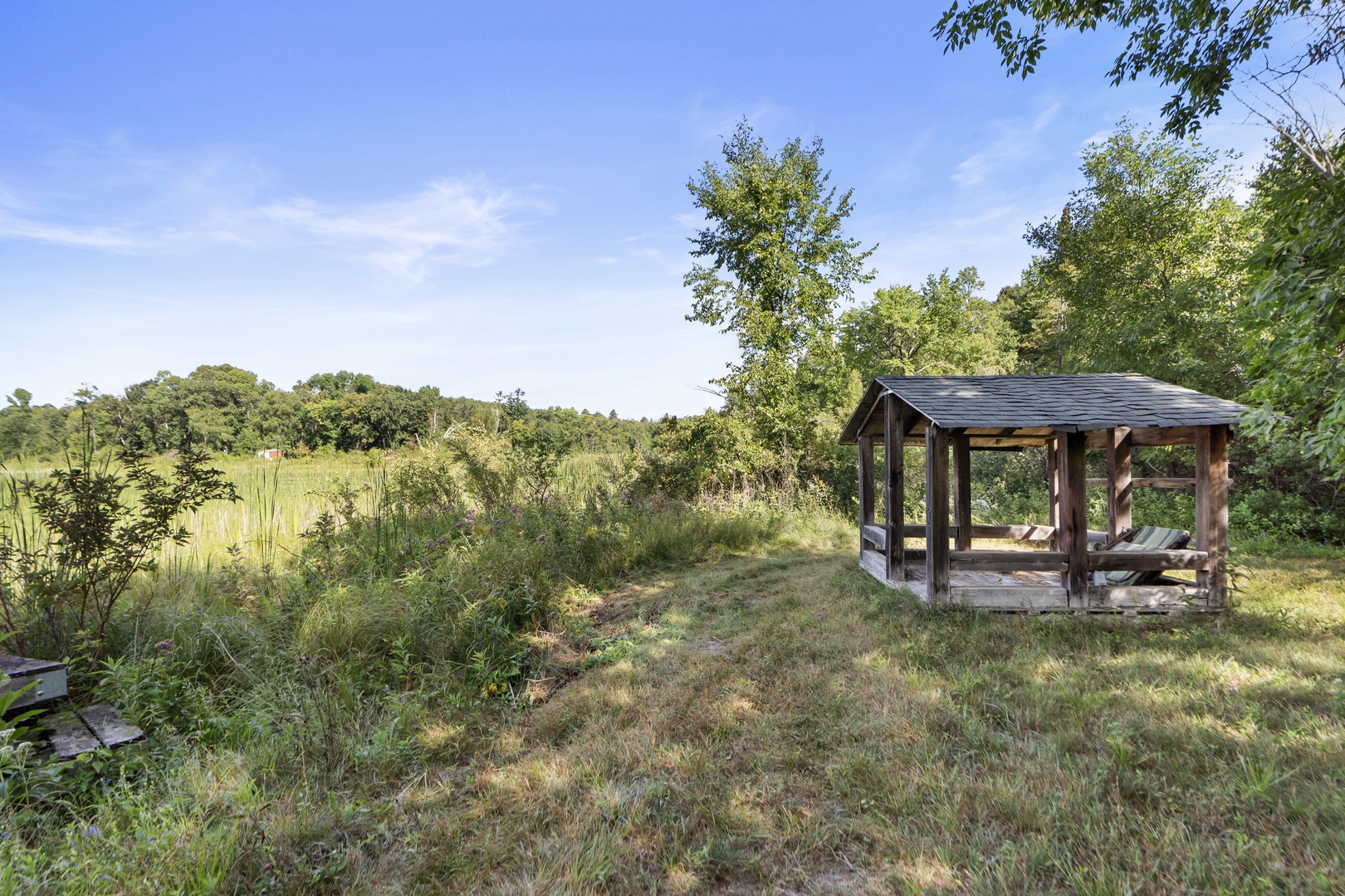 A tranquil covered pavilion nestled among lush greenery and open meadows, offering a peaceful retreat surrounded by natural beauty.