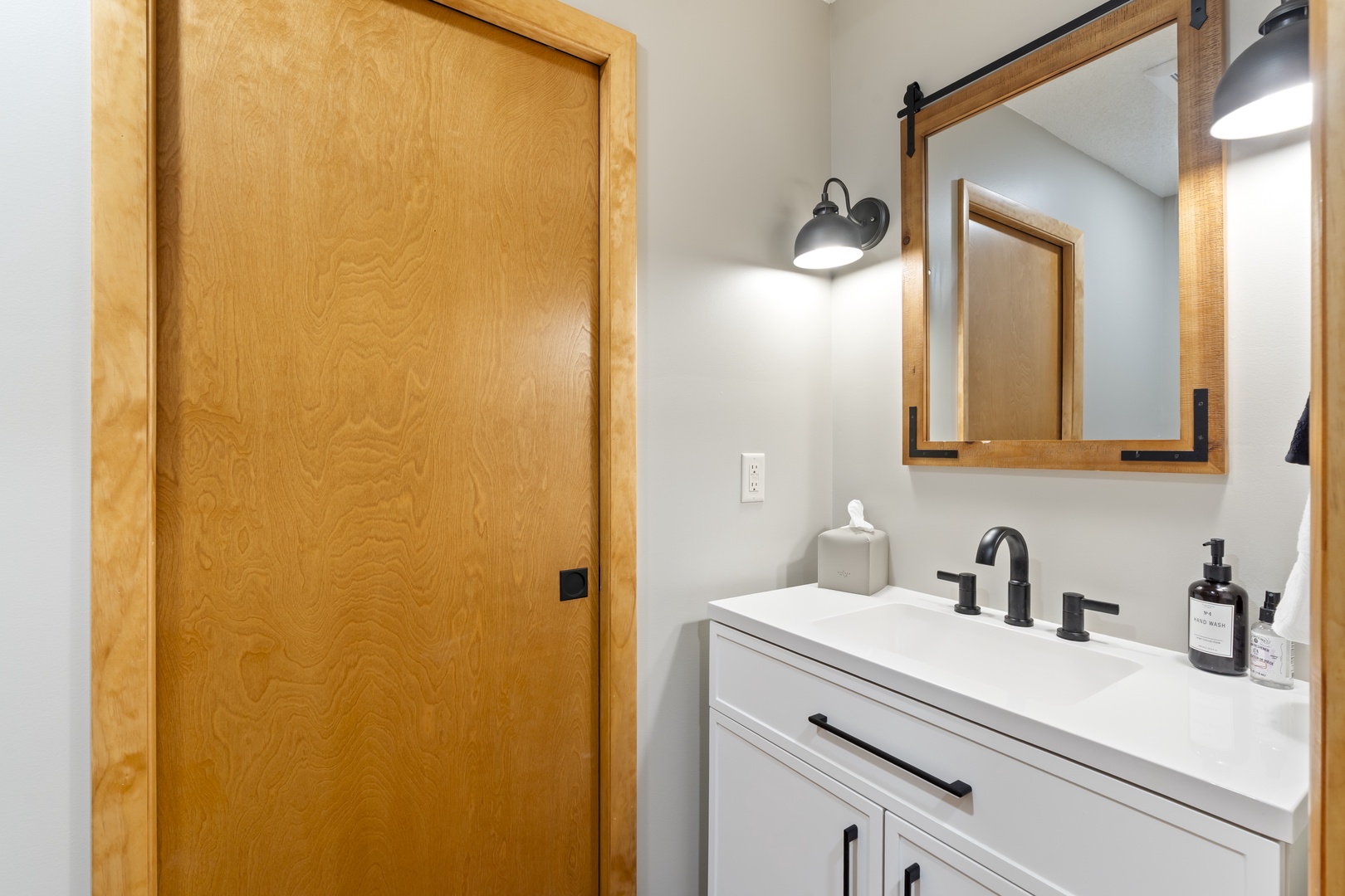 Your stylish bathroom features a modern vanity with sleek black fixtures, warm wood accents, and a sliding barn-door mirror that adds charm and function to your daily routine.