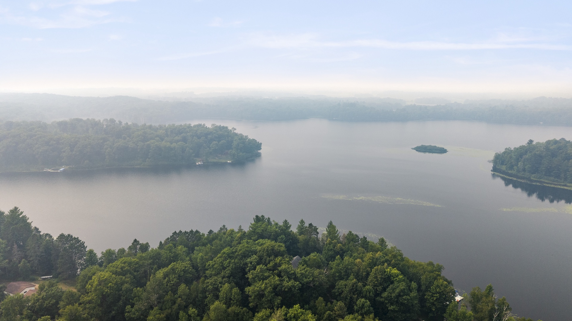 Aerial perspective showcasing the tranquil lake surrounded by forested islands and rolling mountains in the distance.