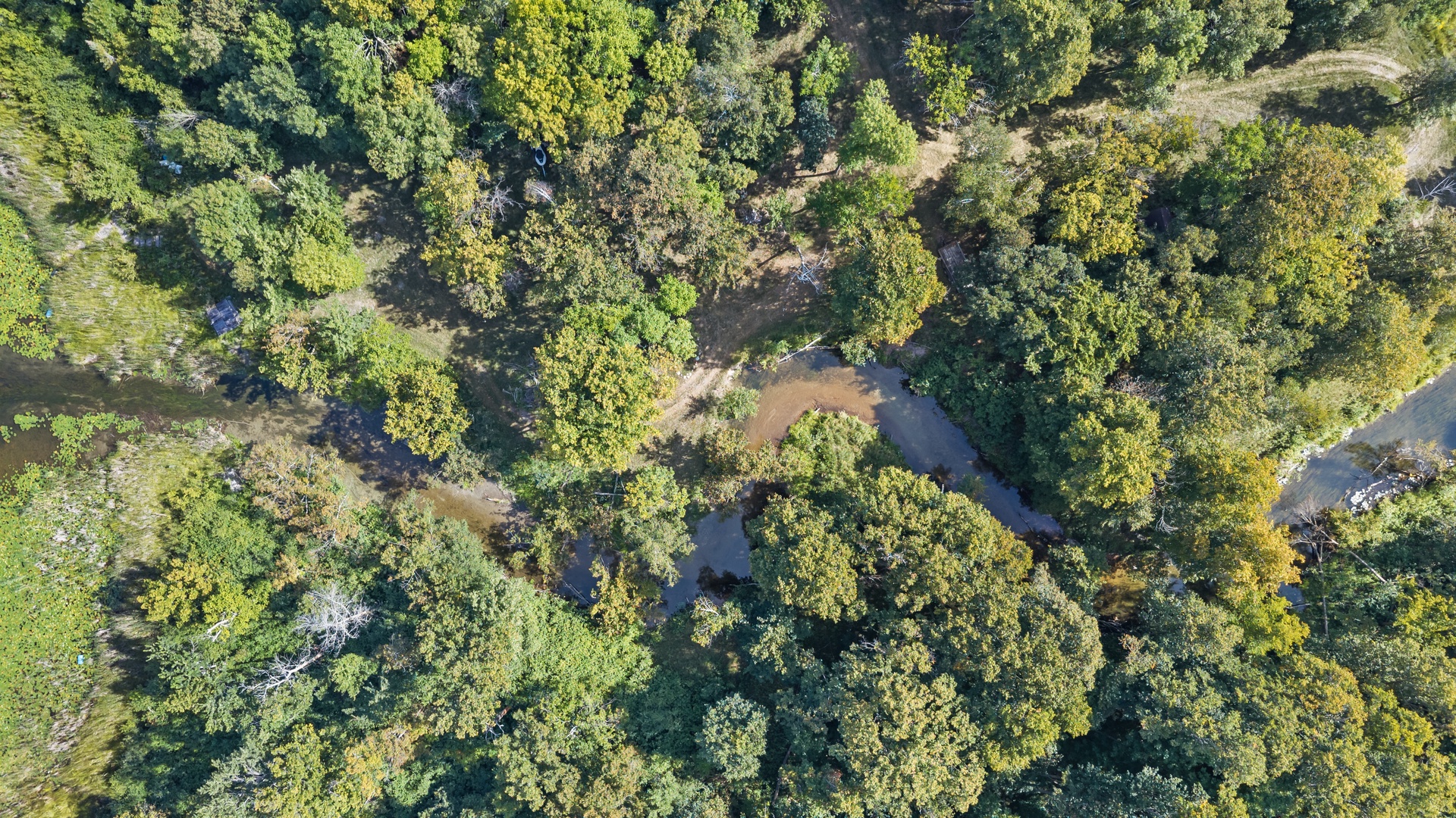 Aerial view of the property surrounded by lush forest canopy and a gentle stream, showcasing the natural landscape and secluded location in the woods.